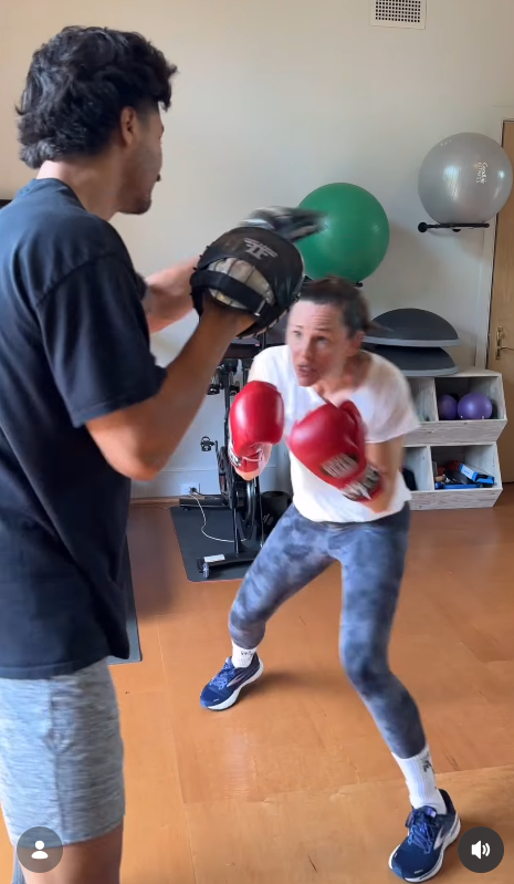 Jennifer Garner crouches slightly and throws punches toward the trainer’s padded mitts in a home workout room filled with fitness balls and equipment. | Source: Instagram/jennifer.garner