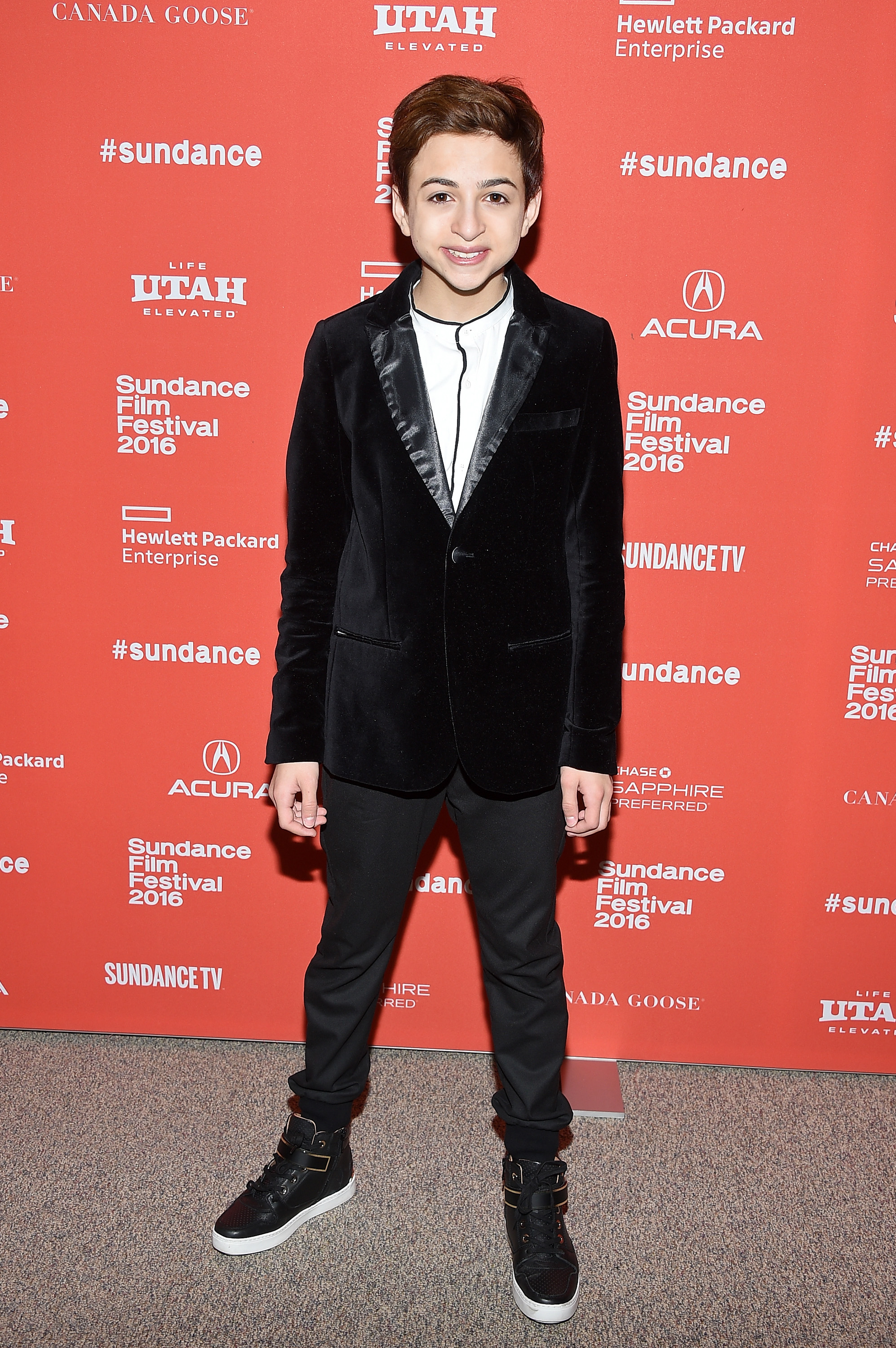 J.J. Totah smiles for photographers at the premiere of Other People during the Sundance Film Festival in Park City, Utah, dressed in a black velvet blazer, a white shirt, black trousers, and high-top sneakers. | Source: Getty Images