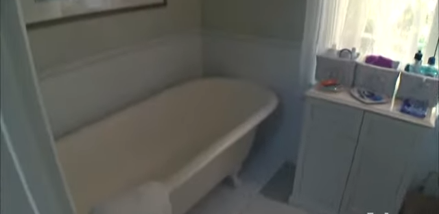 The cozy space features a classic clawfoot soaking tub paired with soft gray storage cabinets. | Source: YouTube/@Biography