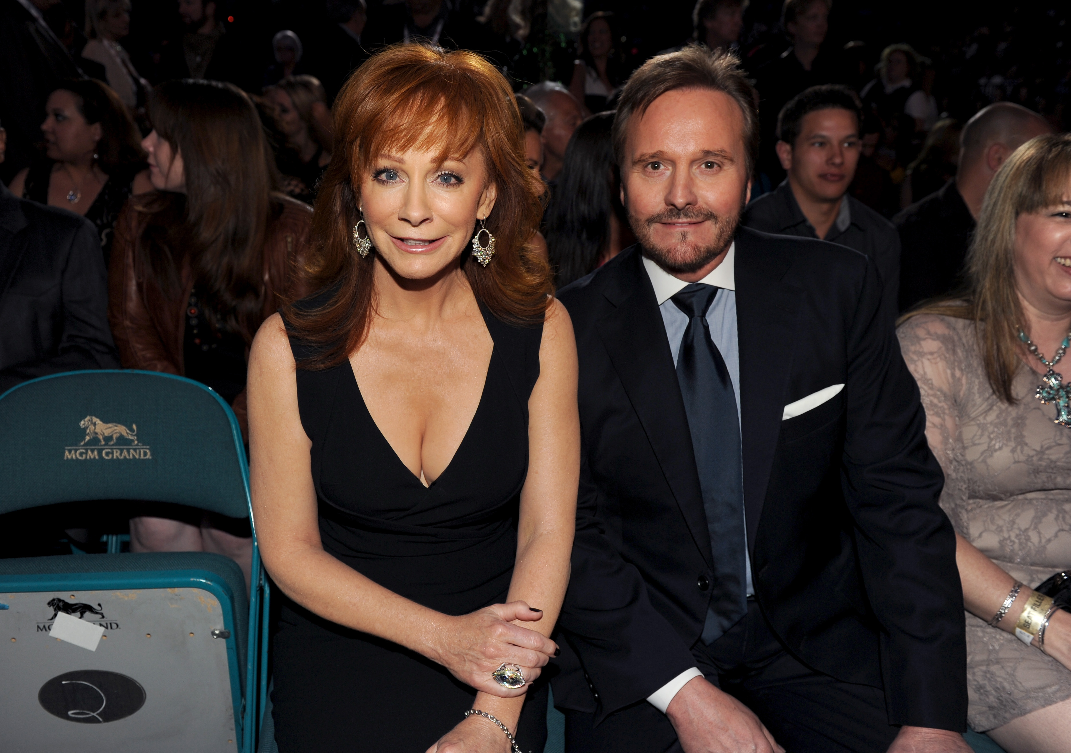 Reba McEntire and then-husband Narvel Blackstock sit together in the audience at the 48th Annual Academy of Country Music Awards at the MGM Grand Garden Arena in Las Vegas on April 7, 2013. The country music star wears an elegant black sleeveless dress with a plunging V-neckline, styled with ornate chandelier earrings and a statement cocktail ring, while Blackstock coordinates in a classic black suit, white dress shirt, and dark blue necktie. | Source: Getty Images