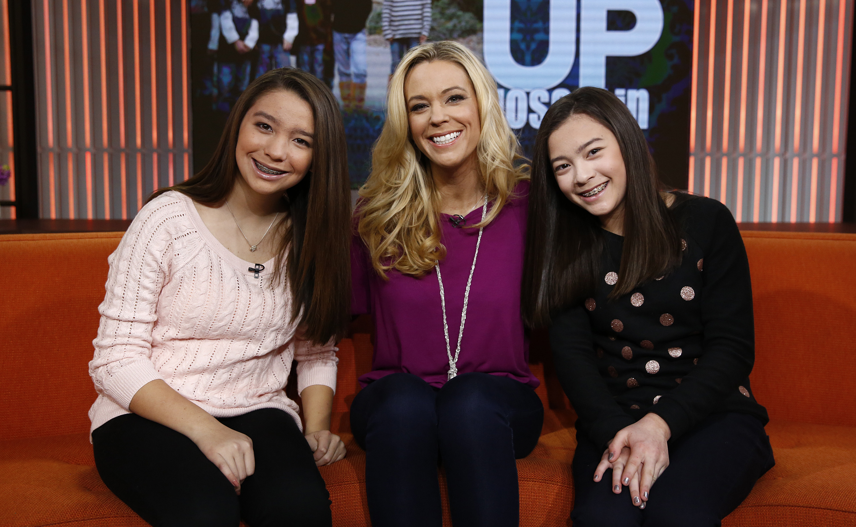 Sitting on a bright orange couch on the "Today" show, Kate Gosselin poses with her twin daughters. In a magenta blouse and long necklace, she smiles warmly, capturing a candid family moment that highlights their close bond.
