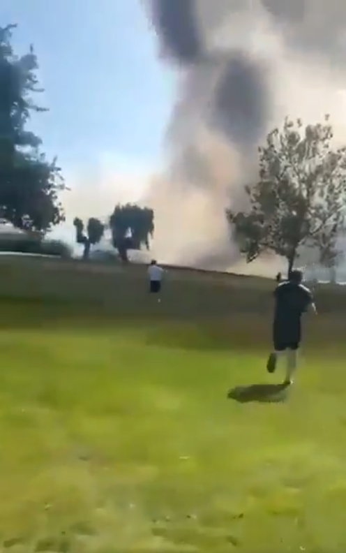 Men running towards the fire and smoke of the crash site, as seen from the golf course. From a video dated July 13, 2025. | Source: X/svsnewsagency