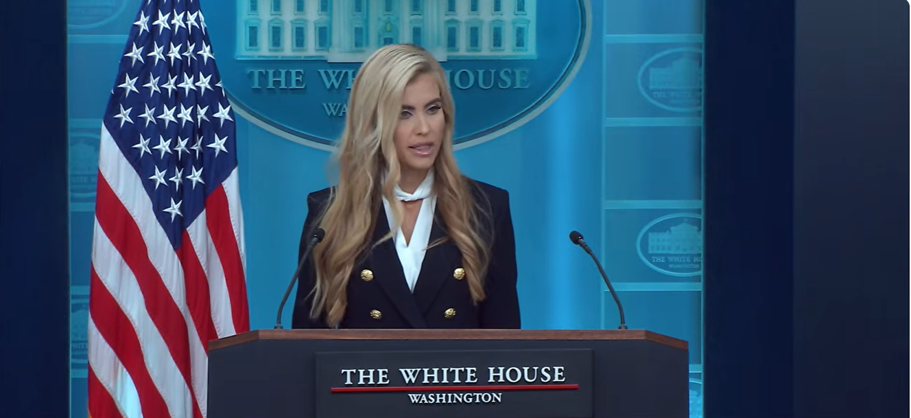 Katie Zacharia looks toward reporters while speaking at the White House briefing podium during her first press briefing, as officials defended her performance despite criticism of her delivery. | Source: YouTube/The White House