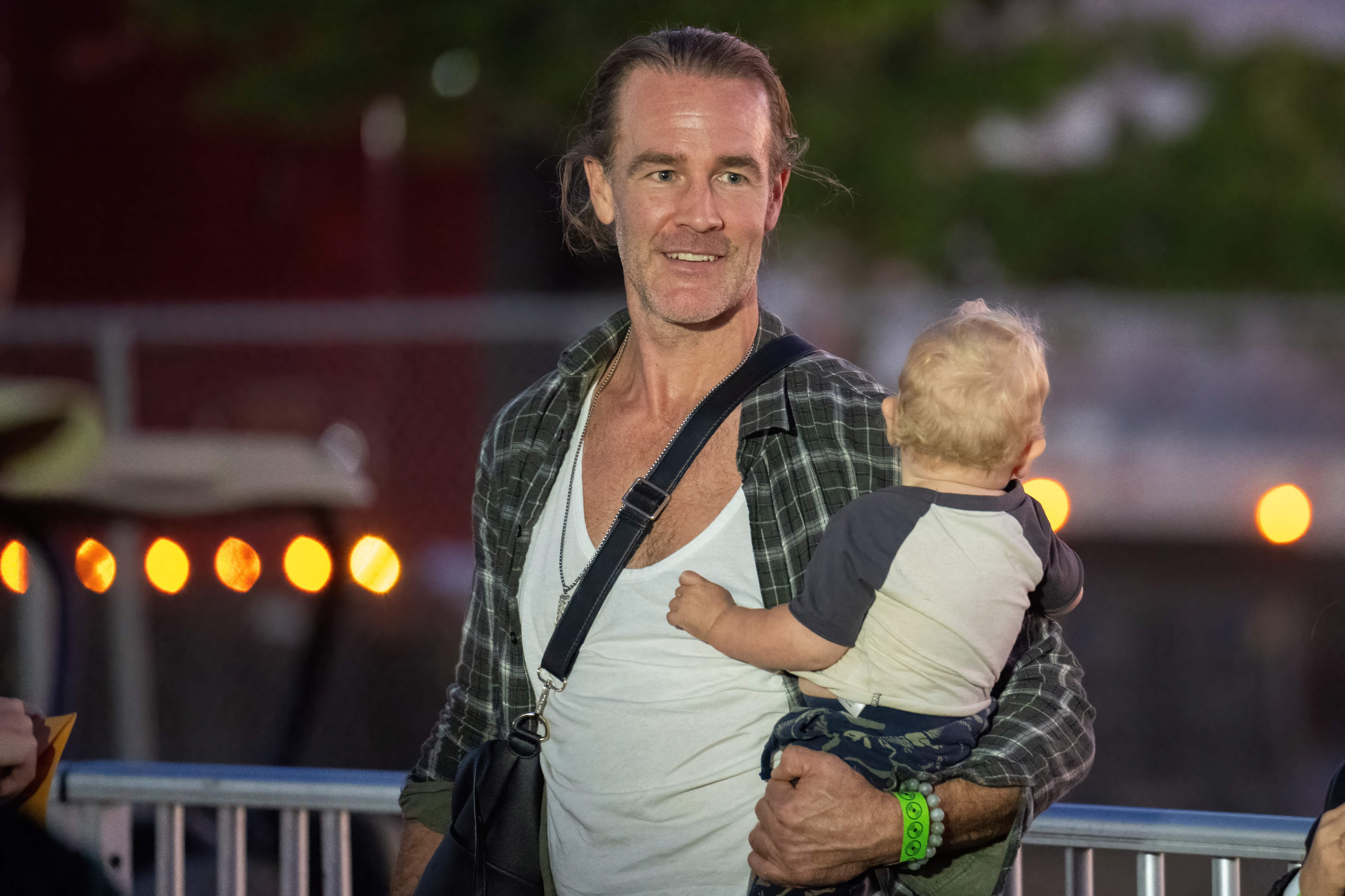 James Van Der Beek arrives at the rock band Green Day's concert in a relaxed flannel and tank, exuding off-duty charm. Holding his child, he blends rock-night energy with warm fatherly ease under the concert lights.