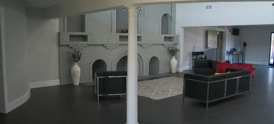 Modern couches and an area rug created a communal seating space beside the repainted brick feature inside the former Tyson estate. Once stripped down and deteriorating, this portion of the mansion was given polished flooring, neutral walls, decorative pieces, and contemporary furniture as Living Word Sanctuary Church reshaped private residential rooms into welcoming areas intended for members of its growing Ohio congregation to gather. | Source: YouTube/WKYC Channel 3