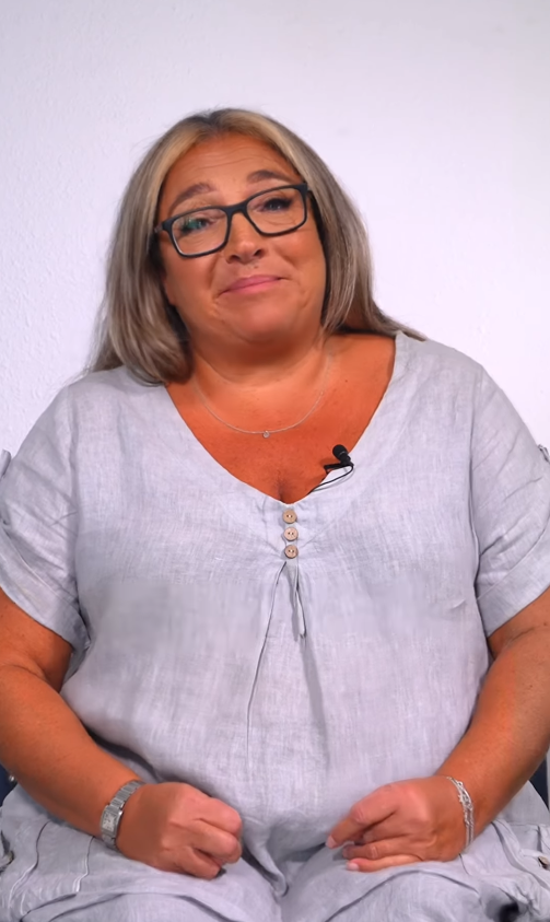 Jo Frost in dark rimmed glasses and a light gray dress with silver bracelets on each wrist. From a video dated July 11, 2025. | Source: Instagram/jofrost