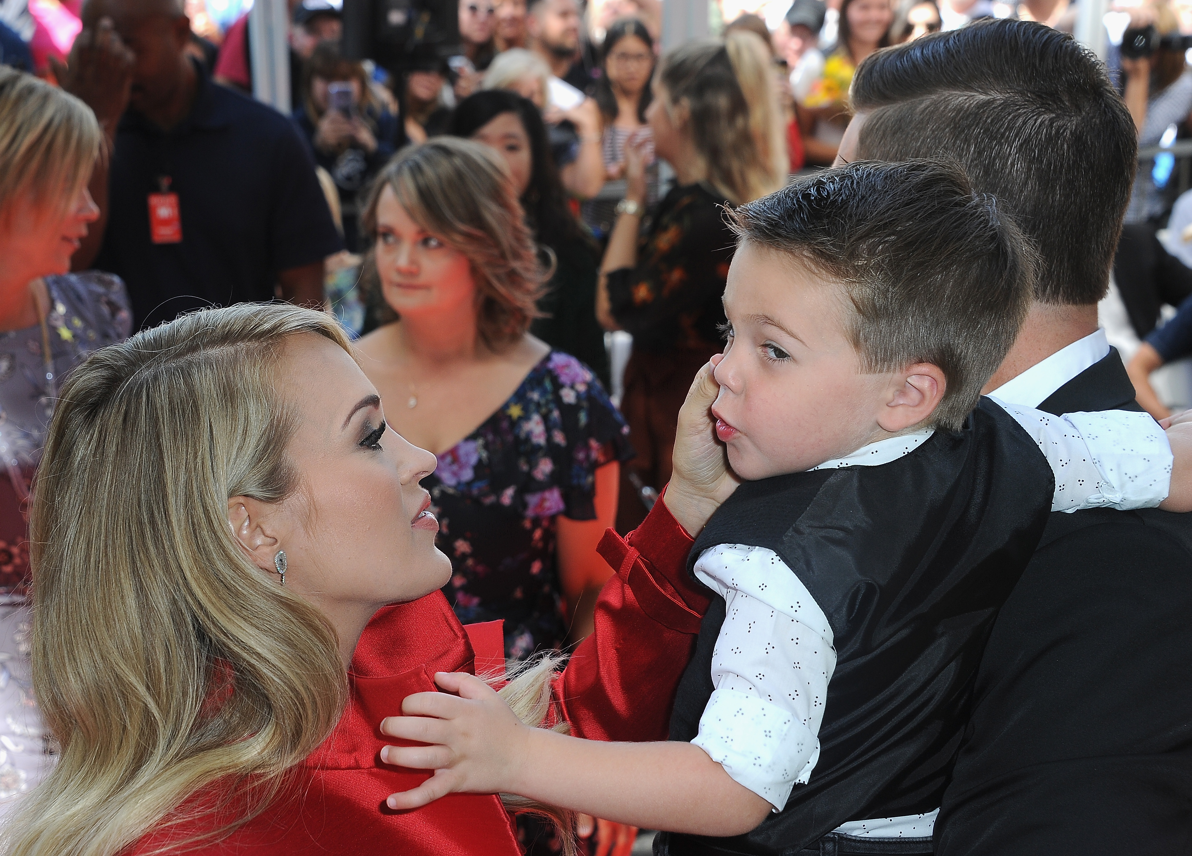 Carrie Underwood shares a tender moment with her eldest son, Isaiah, as her husband, Mike Fisher, holds him at a 2018 event. Carrie and Mike welcomed their second son, Jacob, in January 2019. | Source: Getty Images.