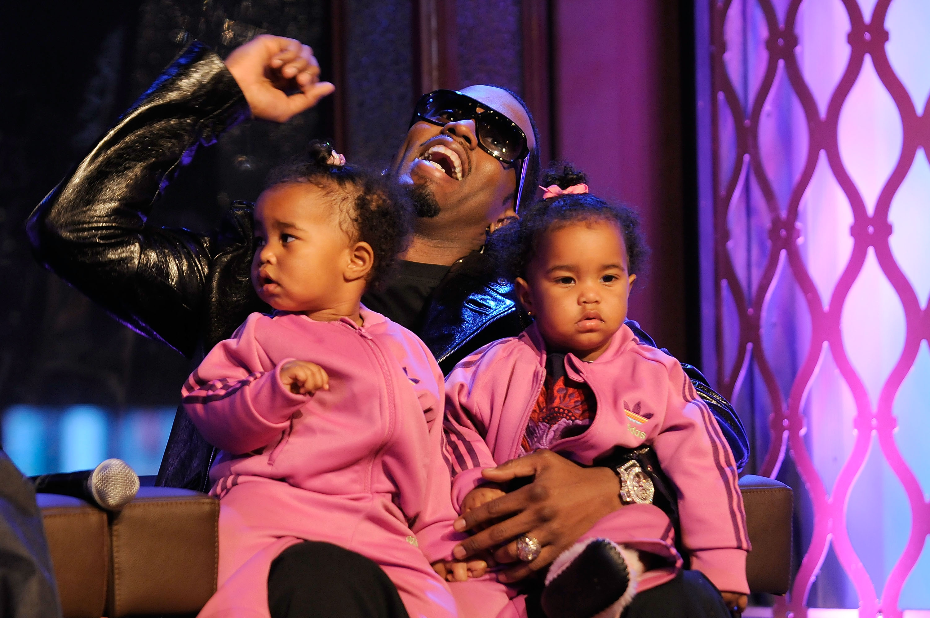 Sean "Diddy" Combs sits onstage with his twin daughters, D’Lila Star and Jessie James Combs, holding them on his lap in matching pink tracksuits during a lively studio taping.