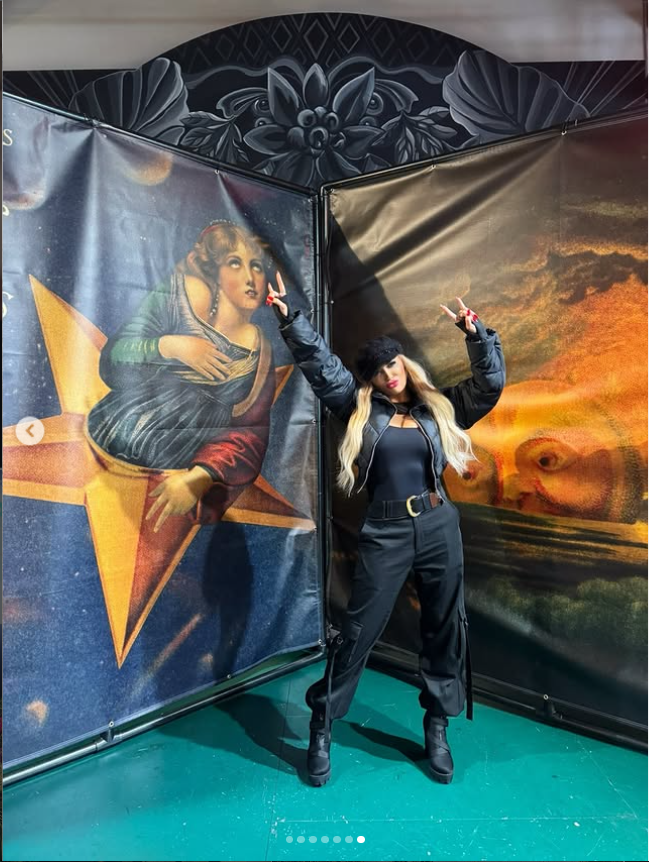 Jennifer Eckhart poses in an all-black outfit during an outing, wearing a black jacket, top and pants with boots as she stands in front of colorful artwork. | Source: Instagram/jennifereckhart