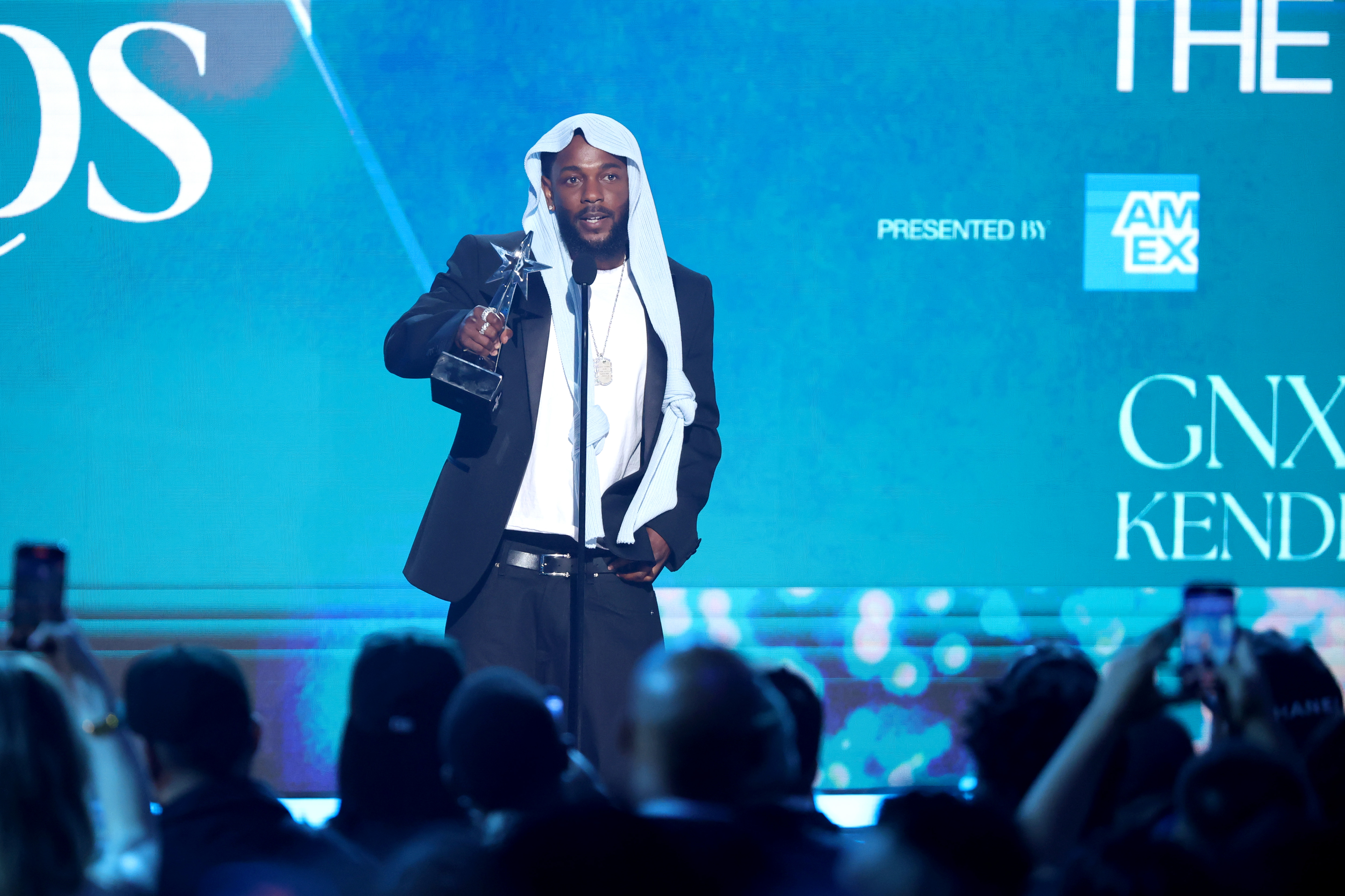 Kendrick Lamar addresses the audience after receiving an award at the 2025 BET Awards in Los Angeles. Wearing a sleek black suit and his viral headpiece, the rapper looked both stylish and reflective in the spotlight.