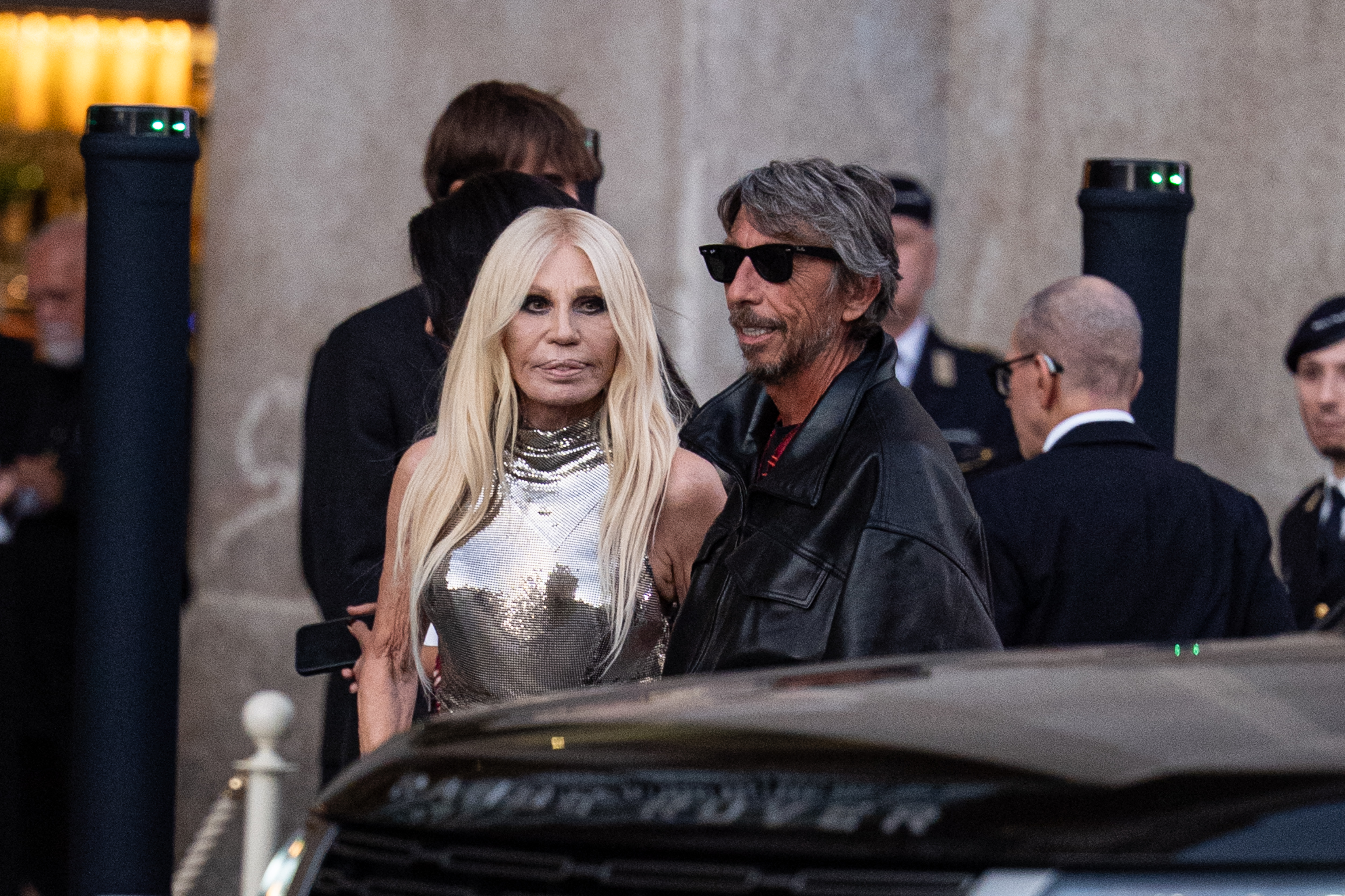 Versace arrives beside Pierpaolo Piccioli, with the closer frame highlighting her reflective silver top and long platinum-blond hair. | Source: Getty Images