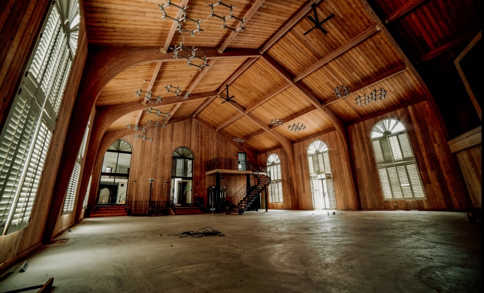 Towering arched windows line a vast wood-paneled hall inside Mike Tyson's former Ohio estate, drawing attention to the property's cathedral-like proportions. Exposed beams span the vaulted ceiling above an otherwise vacant floor, while numerous light fixtures remain in place. The cavernous room was among the mansion's many oversized spaces, which would eventually be adapted for an entirely different purpose. | Source: Facebook/Johnny Joo
