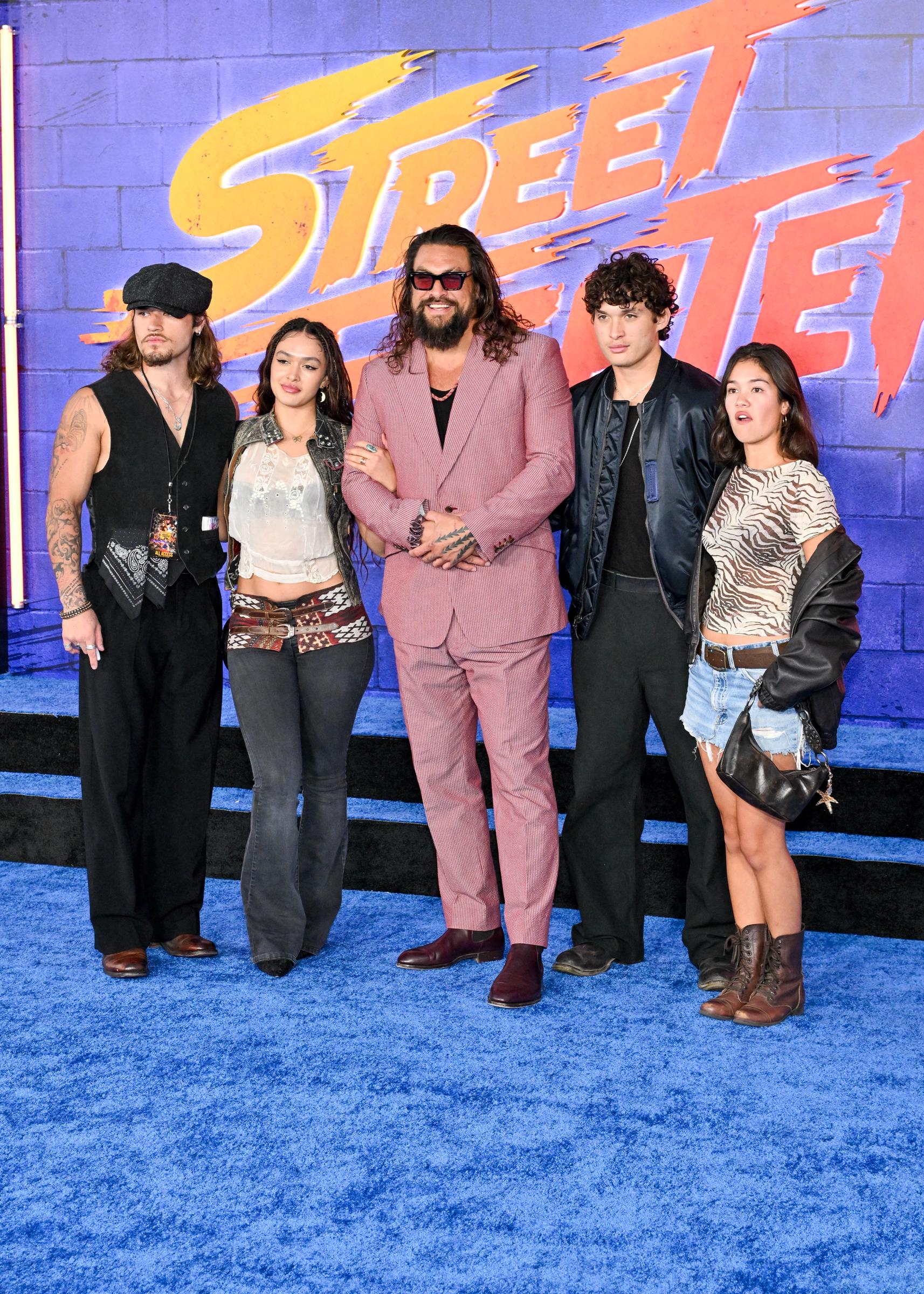 Jason Momoa is flanked by Nui Momoa, daughter Lola Iolani Momoa, son Nakoa-Wolf Momoa, and a companion on the blue carpet at the Los Angeles premiere of Paramount Pictures' "Street Fighter" at the TCL Chinese Theatre on October 12, 2026, in Hollywood, California. The group presents a coordinated, eclectic street style, with Lola holding her father's arm in a sheer lace crop top and low-rise dark flares accented by a wide pattern belt, while Nakoa-Wolf stands tall in an open satin bomber jacket and relaxed black slacks. | Source: Getty Images