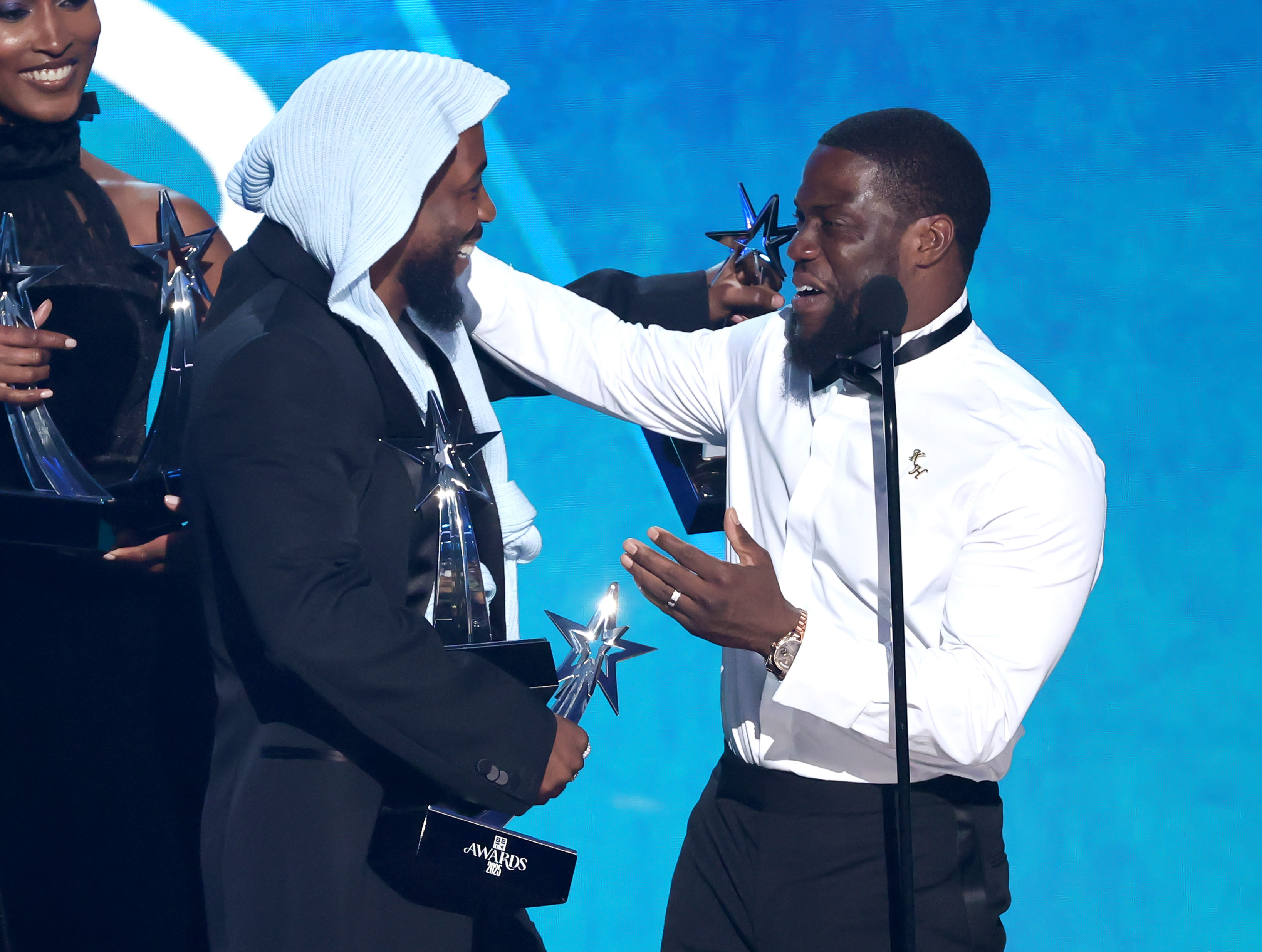 Kevin Hart shares a laugh with Kendrick Lamar while handing over one of the artist's many awards during a playful exchange onstage at the 2025 BET Awards. Lamar's hands were already full of trophies by this point in the show.