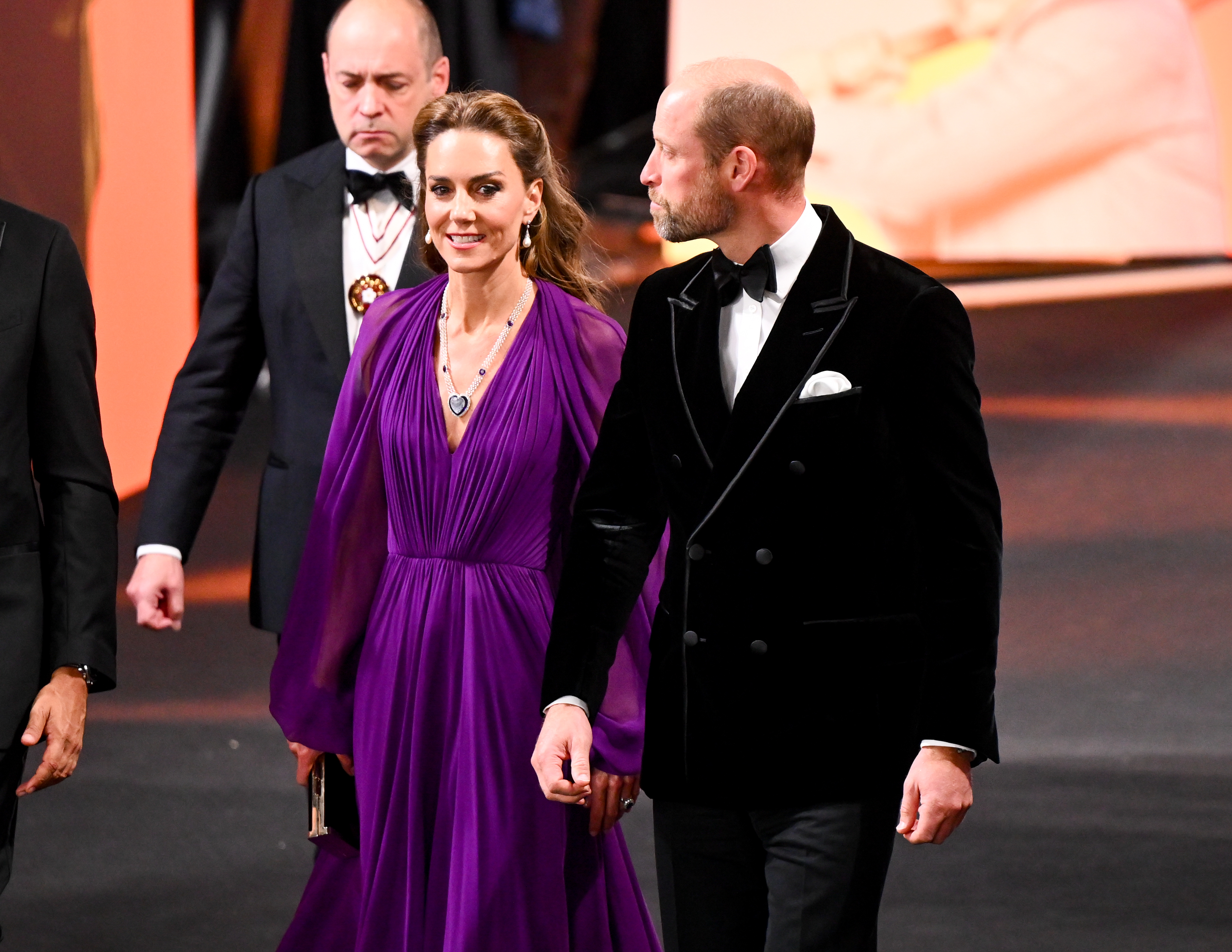 Catherine and William are pictured together at the "Digger" global premiere in London. Catherine wears her floor-length purple gown with a plunging neckline and dark pendant necklace, while William appears in black tie.