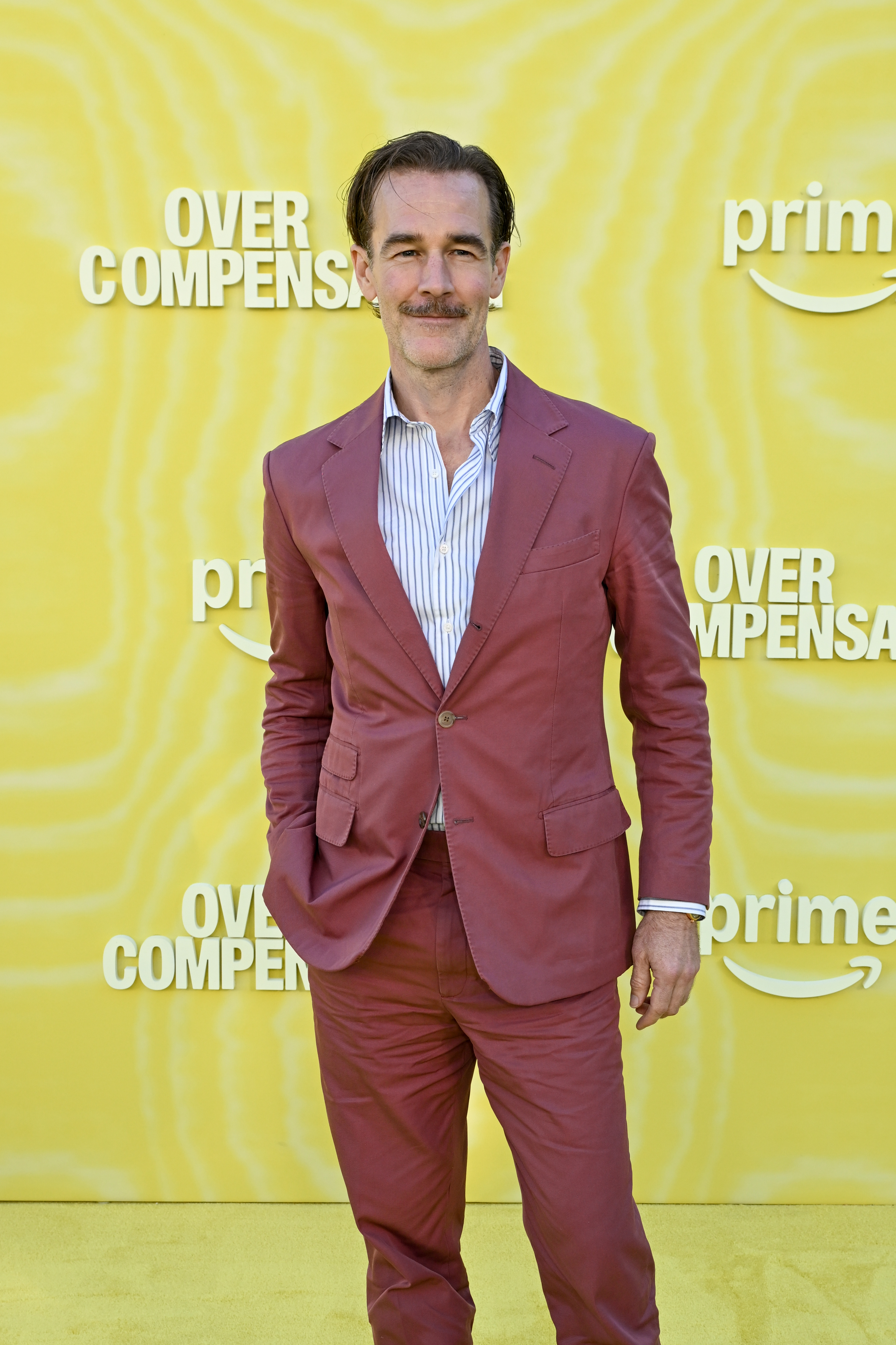 James Van Der Beek steps onto the yellow carpet in a dusty-rose suit that mirrors his effortless confidence and wry charm. His neatly trimmed mustache and relaxed stance give him a cool, vintage edge against the bright backdrop. At the "Overcompensating" premiere, he radiates easy sophistication with a hint of playful swagger.