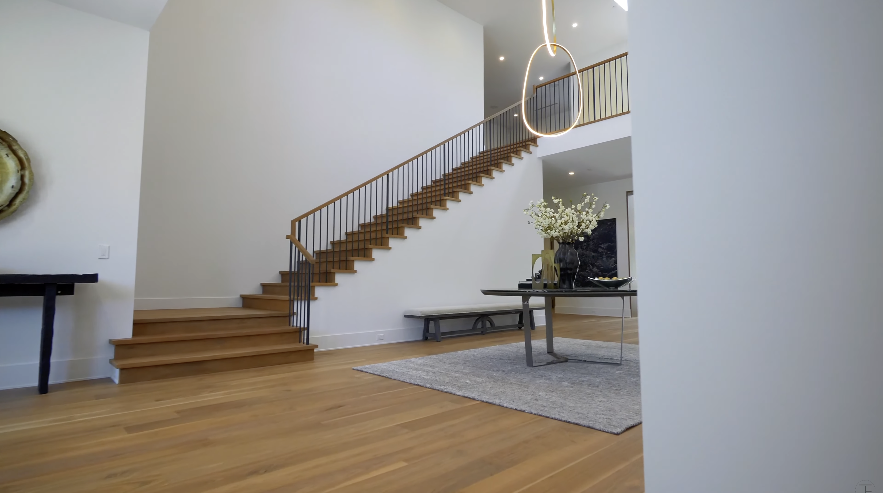 Wood treads climb toward the open upper gallery, with black metal balusters providing contrast against the white walls. The restrained finishes leave the staircase as the main architectural feature in this view. | Source: Youtube/Tomer.Fridman
