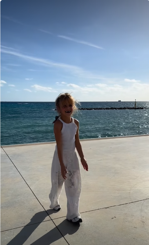 Jake Hall’s daughter, River, smiles while walking along a seaside promenade in a white outfit. | Source: Instagram/jakehall
