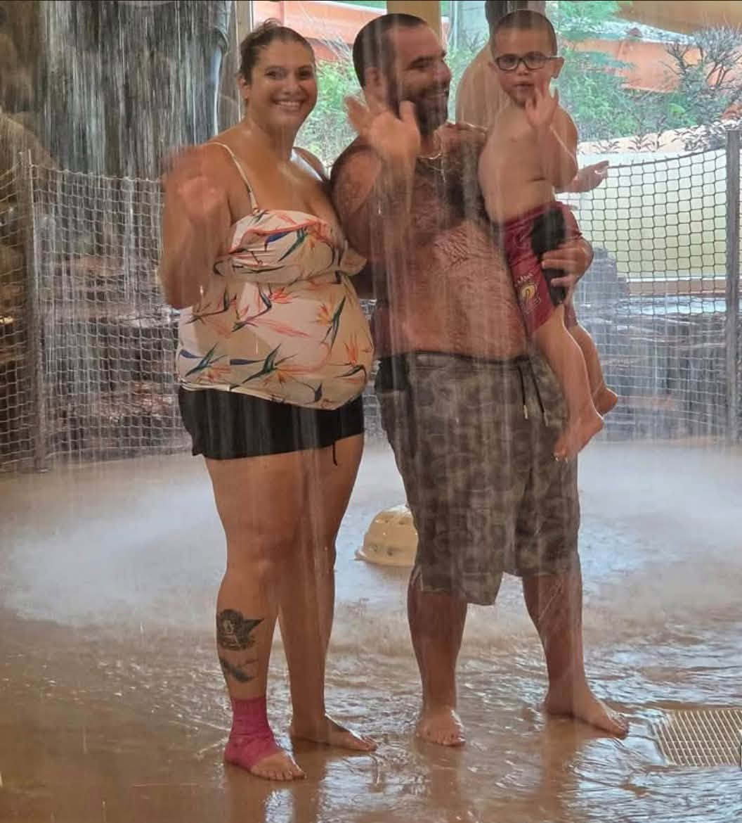 The Harrison family smiles and waves beneath an indoor waterfall at a water park, in a poignant image of the father and son whose lives ended in tragedy. | Source: Facebook/TrueCrimeMama