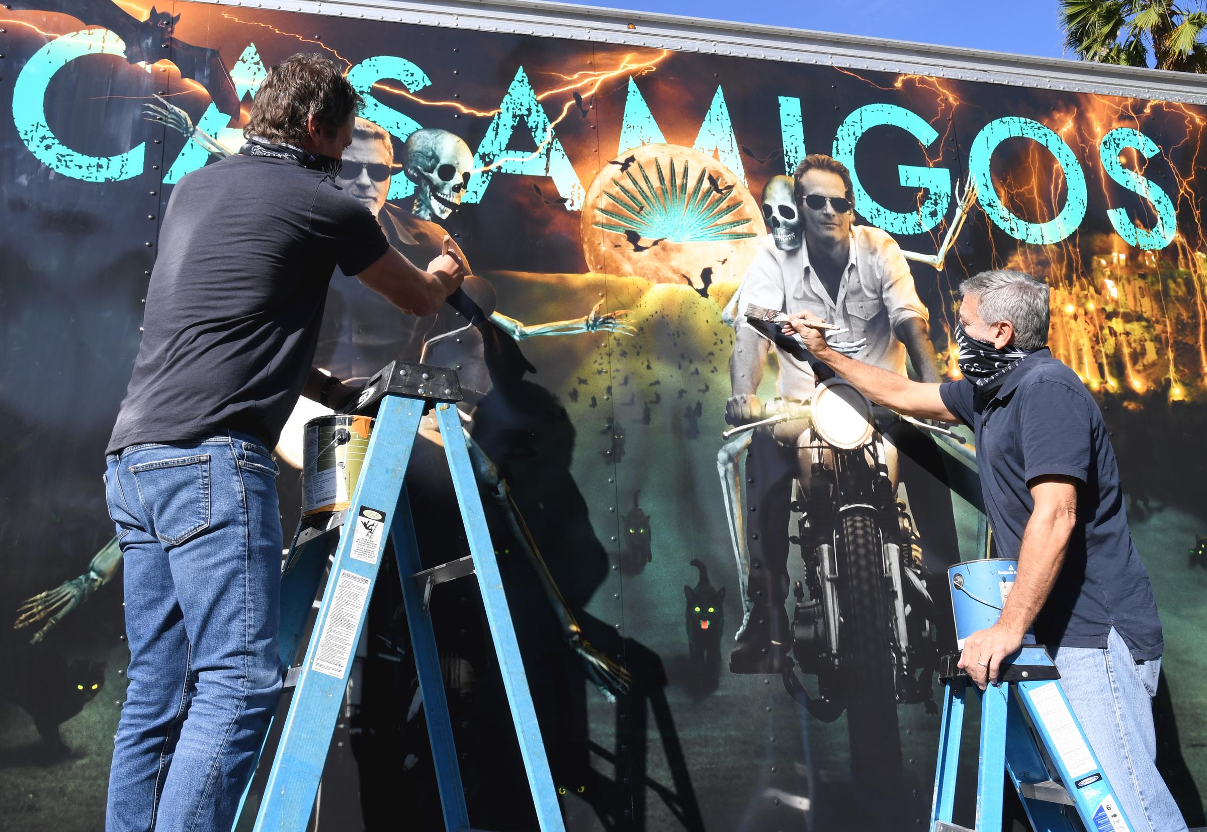 Casamigos co-founders Rande Gerber and George Clooney got hands-on ahead of the spooky season on October 30 in Los Angeles, California. Perched on blue step ladders in matching casual tees, jeans, and neck gaiters, the longtime business partners held paintbrushes and cans to put finishing touches on an elaborate Halloween-themed truck mural featuring their motorcycle-riding likenesses and skeletal art. | Source: Getty Images