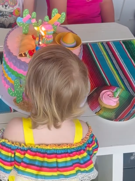 Kaliyah stands in front of a colorful birthday cake decorated with cactus shapes and a miniature sombrero. Her rainbow-striped dress complements the decorations, adding a festive family moment to the ranch photographs. | Source: Instagram/wynonnajudd