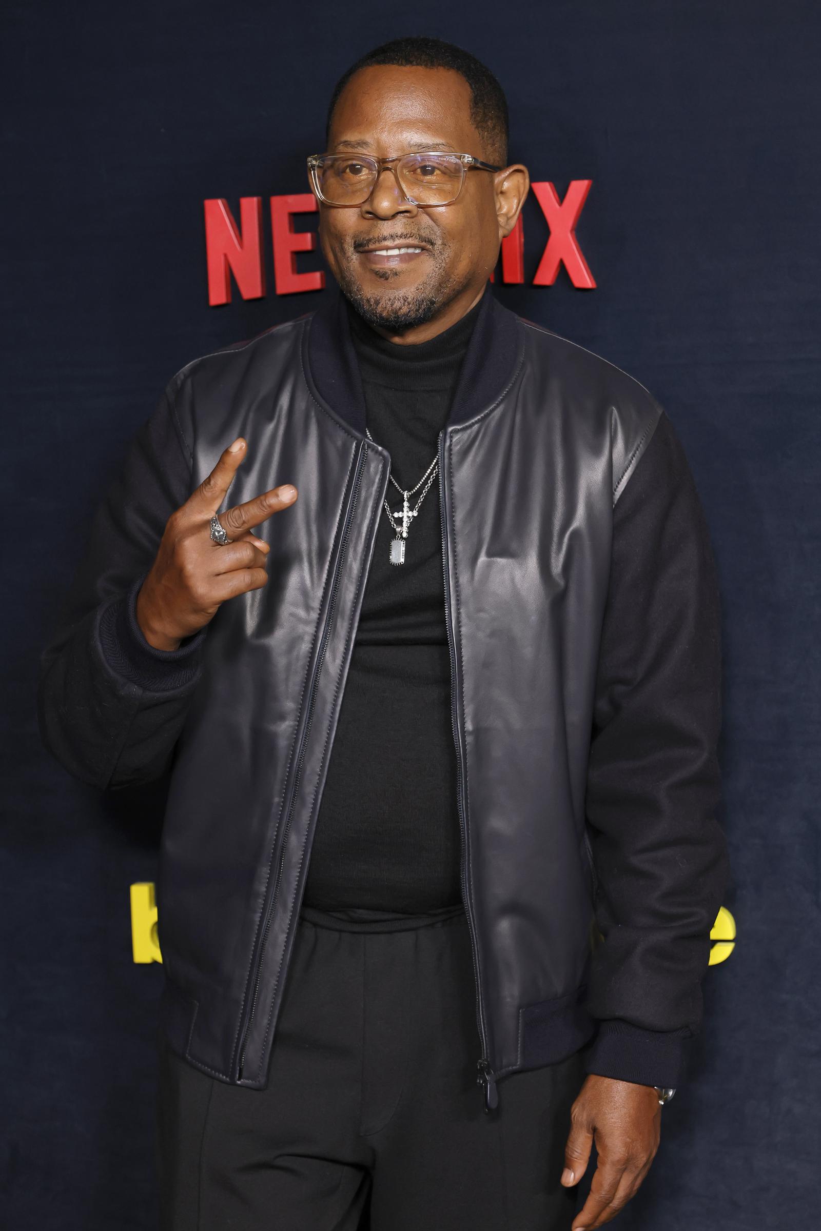 At the premiere of Netflix’s "Being Eddie," Martin Lawrence poses in a black leather jacket and glasses. With a calm expression and relaxed stance, he looks directly toward the camera against the event backdrop.