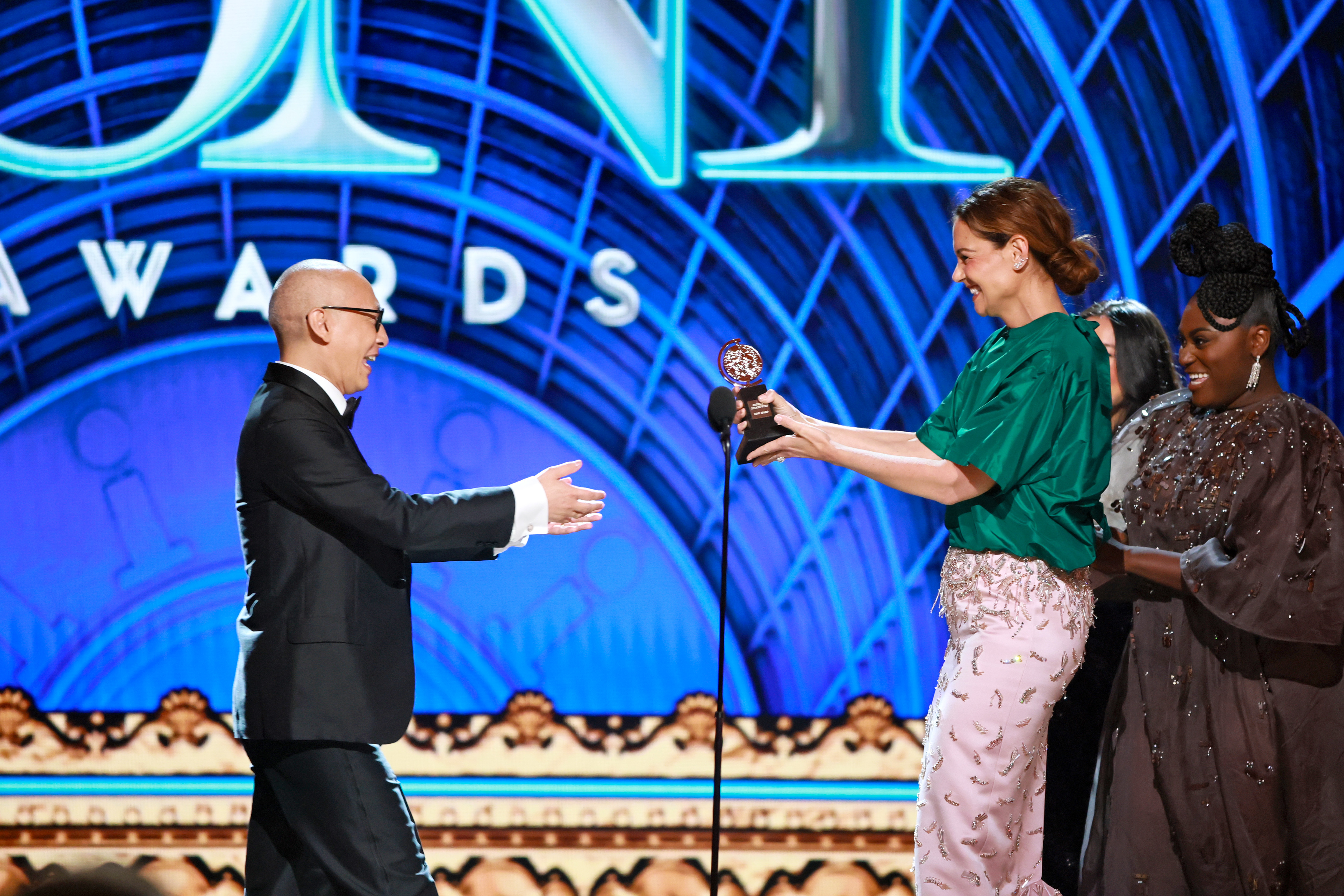Francis Jue receives his Tony Award for Best Featured Actor in a Play from Katie Holmes and Danielle Brooks. Holmes beams as she hands over the trophy, marking one of the ceremony's most heartfelt moments.