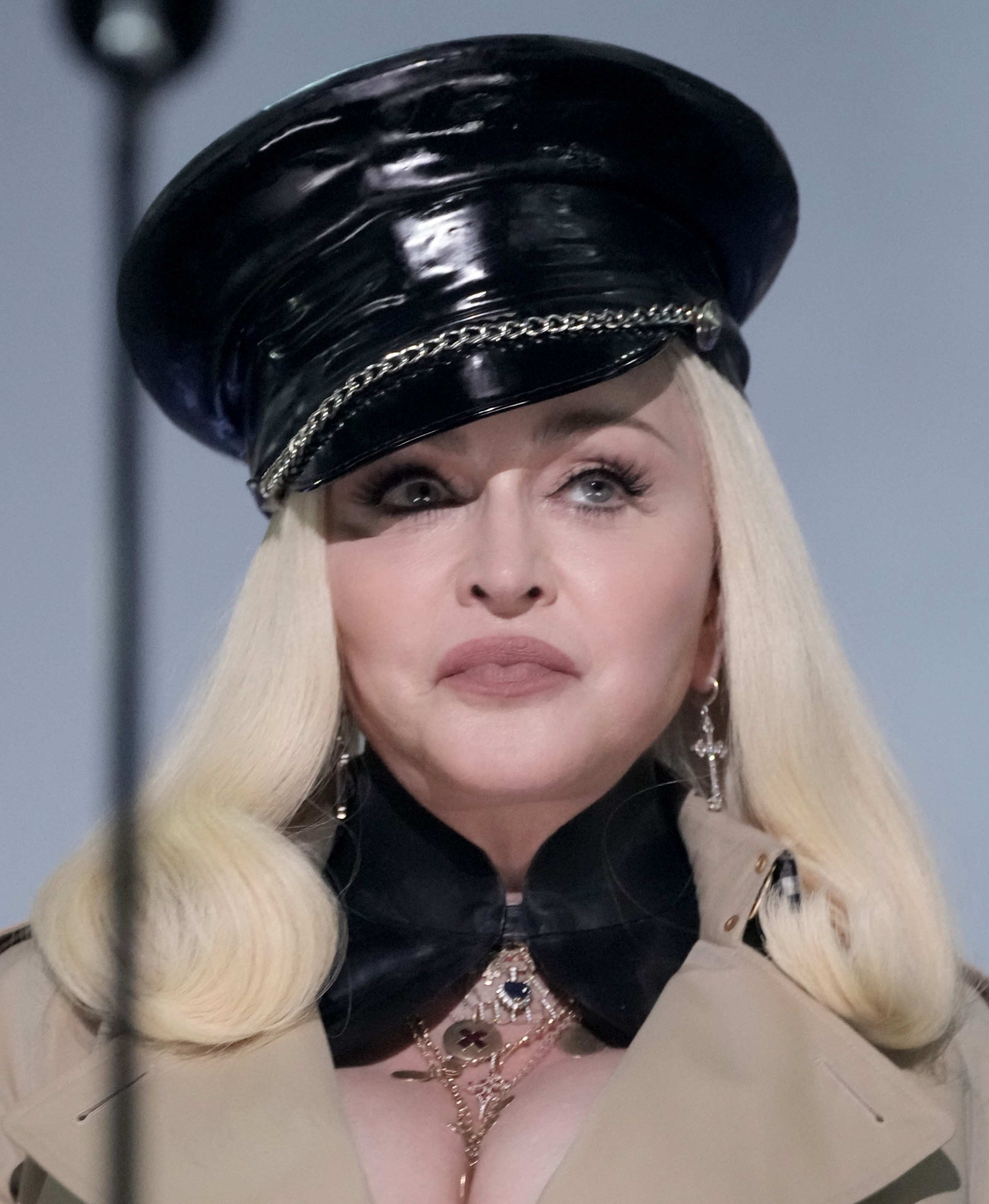 Madonna appears in a glossy black cap with chain detailing, long platinum-blond hair, dangling earrings and layered clothing and jewelry. | Source: Chat GPT