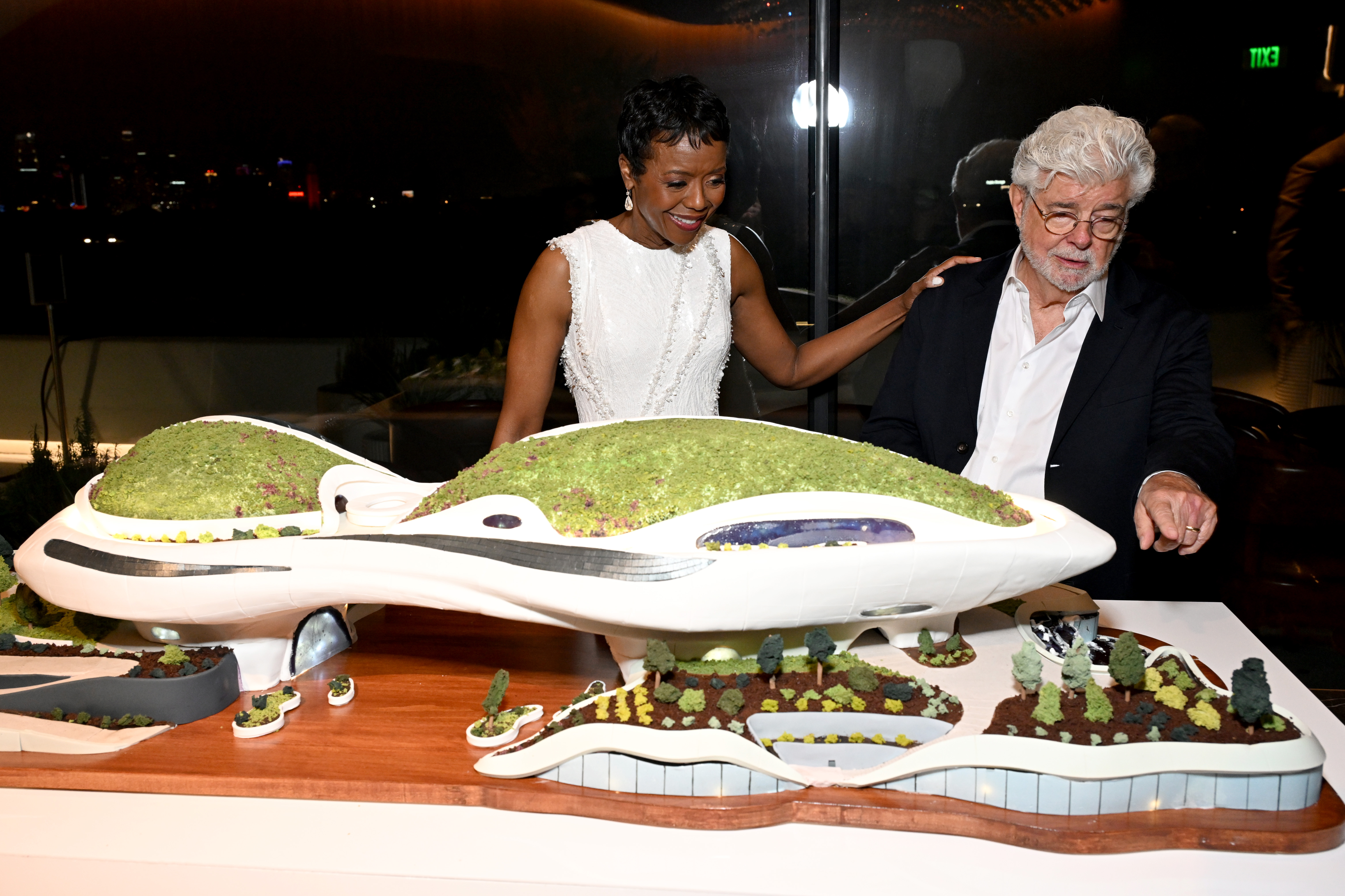George Lucas and Mellody Hobson stood together beside a detailed model of the Lucas Museum and its landscaped grounds. Hobson rested a hand on Lucas' shoulder as the co-founders viewed the display. | Source: Getty Images