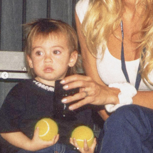 In an intimate retro snapshot, a young Dylan Jagger Lee sits clutching two yellow tennis balls while his mother Pamela Anderson rests an affectionate arm beside him, wearing a white tank and blue trousers. Reflecting on her motherhood journey during the holidays, she celebrated the deep foundation of love that anchors her life: "The love…and pride I feel - as a mother to the sweetest Brandon and Dylan… My love story is not complete without them. 🤍" | Source: Instagram/pamelaanderson