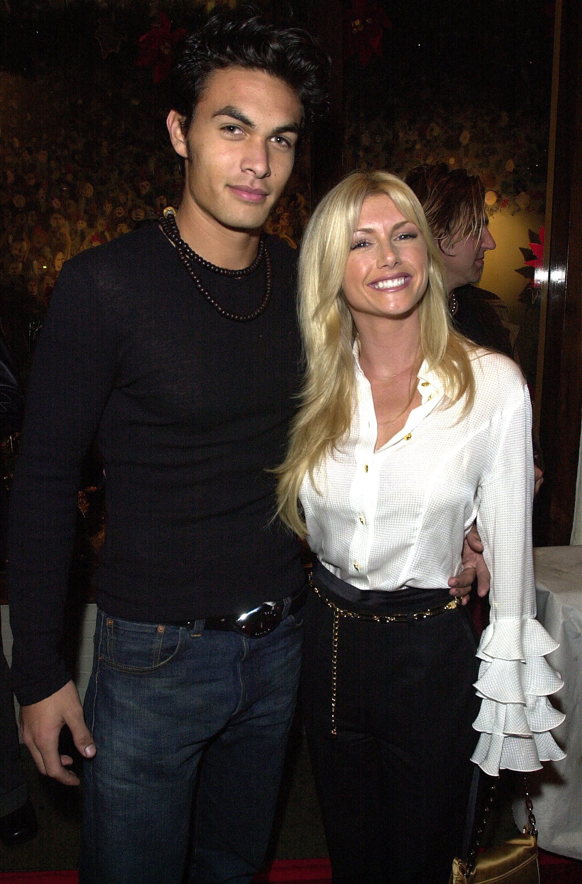 Jason Momoa and fellow "Baywatch" cast member Brande Roderick attend an after-party for the My VH1 Music Awards at the Hard Rock Cafe on November 30, 2000, in Los Angeles, California. Momoa sports a long-sleeved black top, dark beaded necklace, and jeans with a statement buckle, smiling alongside Roderick, who pairs a white blouse featuring dramatic tiered ruffled cuffs with high-waisted black trousers and a gold chain belt. | Source: Getty Images