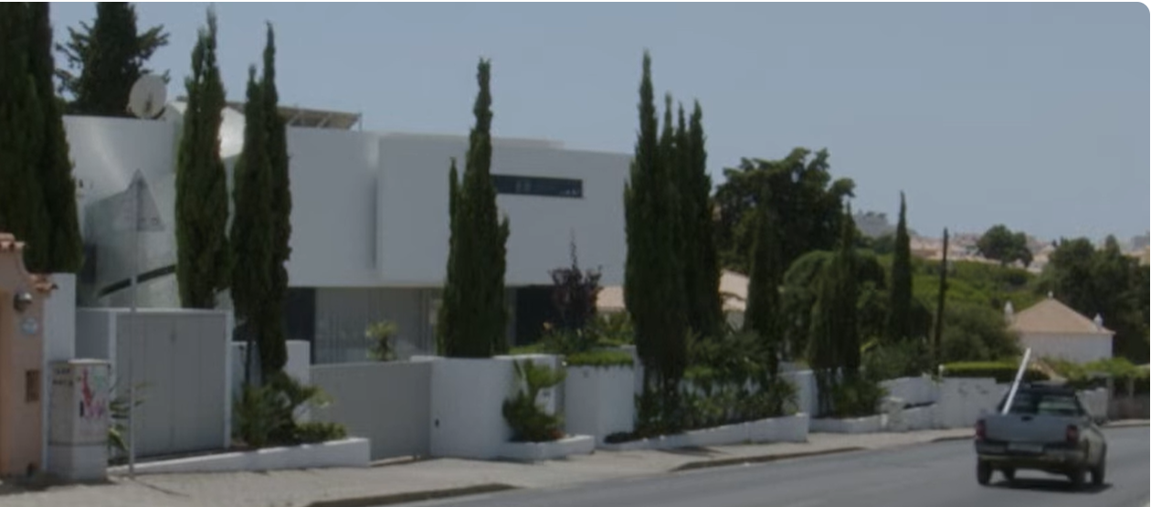 Bonnie Tyler’s modern Portugal home stands behind white boundary walls and rows of tall cypress trees, its crisp geometric design overlooking a quiet, sunlit residential road. | Source: YouTube/AFP News Agency