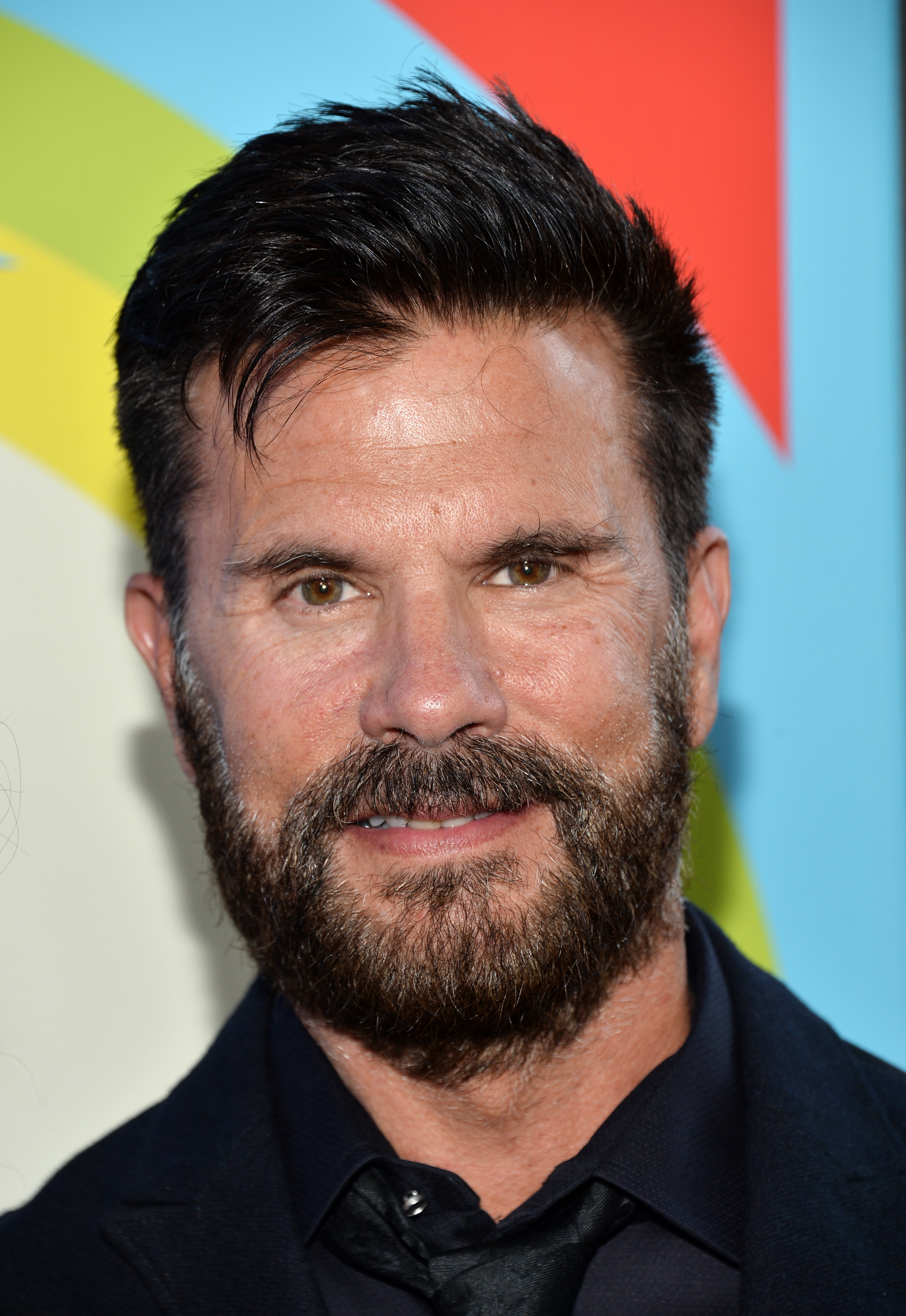 Lorenzo Lamas attends the Los Angeles premiere of "Love & Mercy" at the Samuel Goldwyn Theater in Beverly Hills, California, on June 2, 2015. Smiling closely toward the camera, the actor pairs a full, salt-and-pepper beard and cropped, textured dark hair with a sharp black shirt, matching tie, and tailored suit jacket. | Source: Getty Images