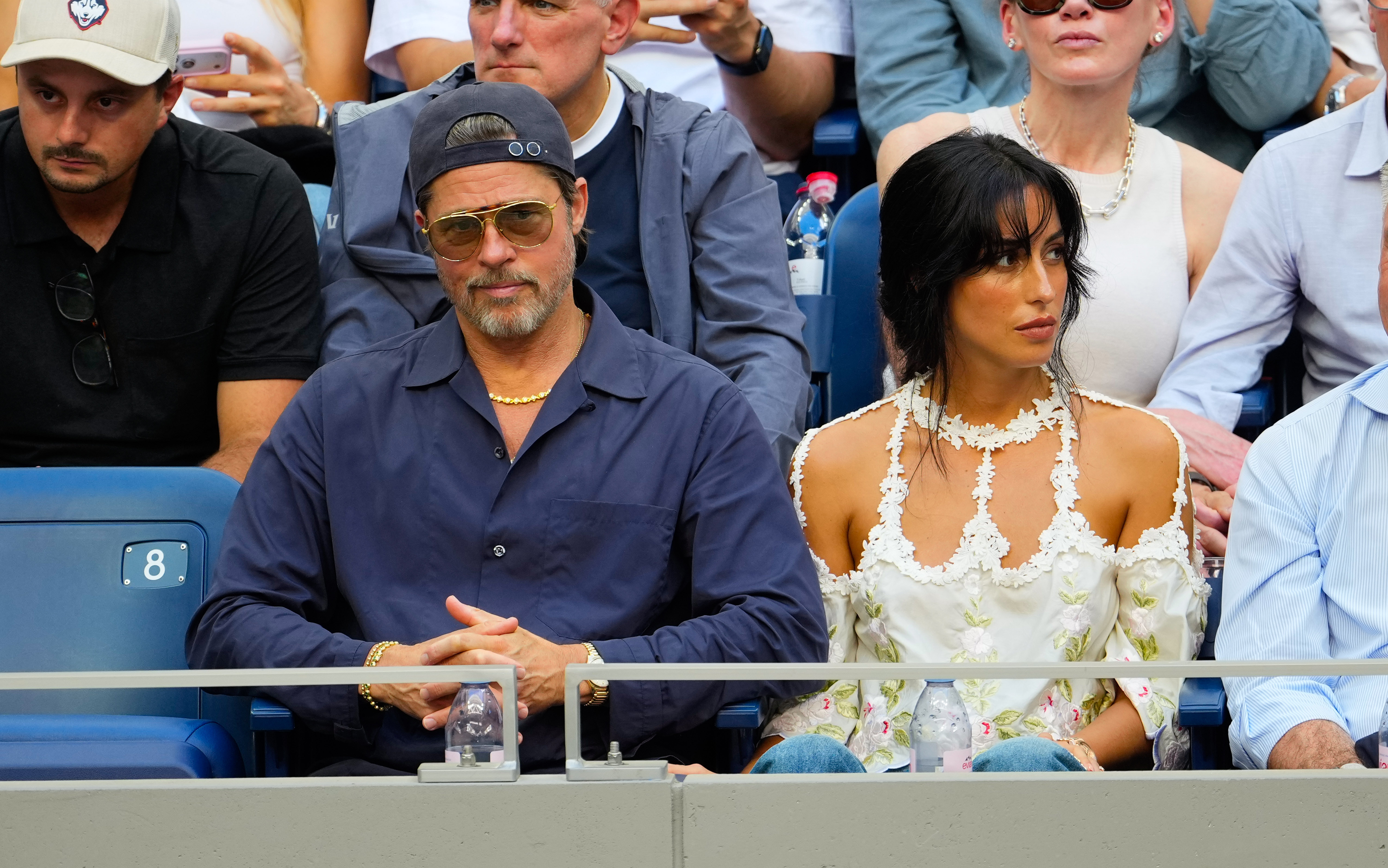 Pitt and de Ramon sat side by side as they followed the men's final in New York City. De Ramon wore her dark hair in a loose updo with face-framing bangs, while Pitt added a gold necklace to his navy look.