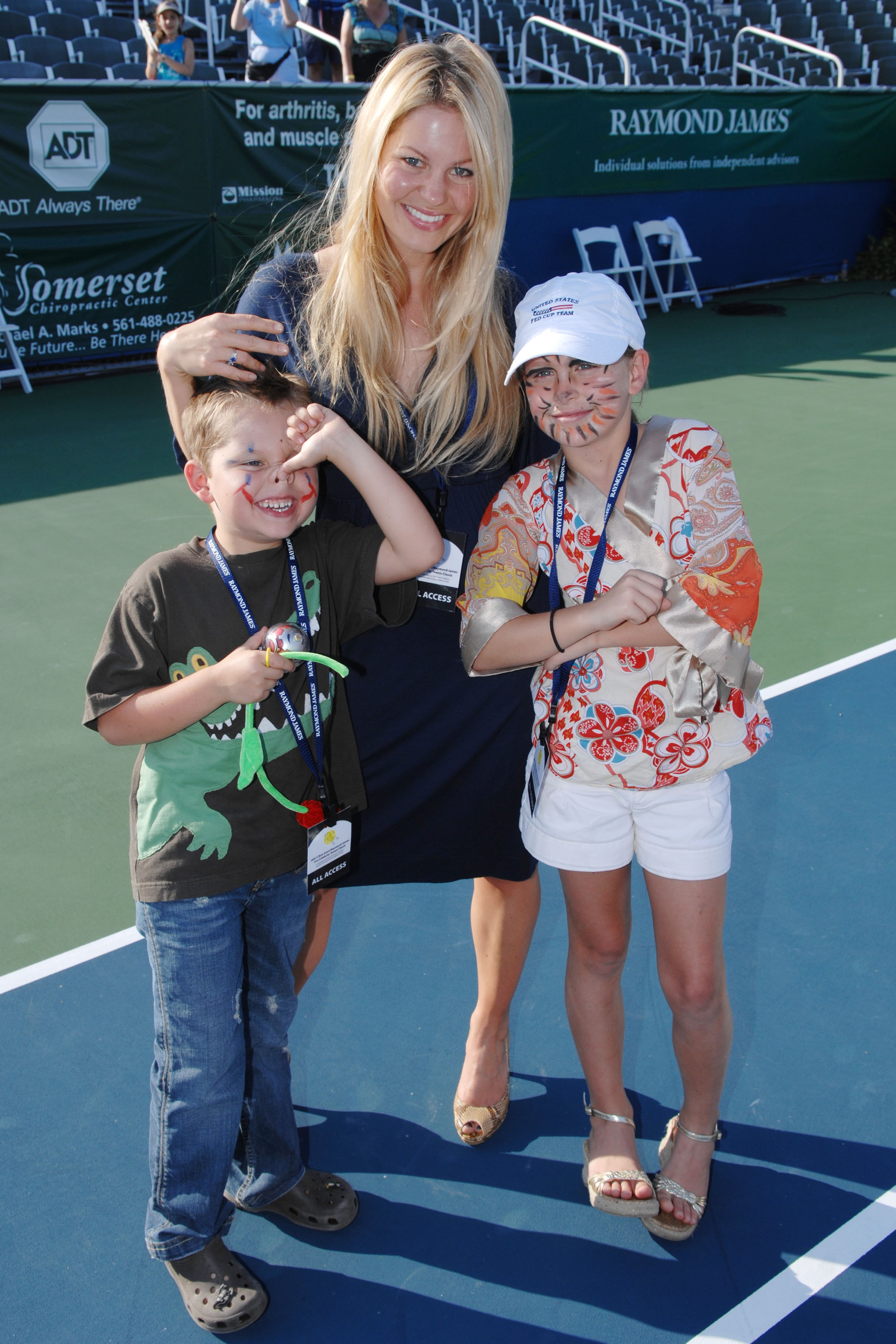 Candace Cameron Bure poses on the court with her children, daughter Natasha Bure and younger son Maksim Bure, during the Chris Evert/Raymond James Pro-Celebrity Tennis Classic at the Delray Beach Tennis Center on November 4, 2007, in Delray Beach, Florida. The proud mother smiles in a navy dress and peep-toe heels alongside her face-painted kids, with little Maksim wearing a graphic dinosaur tee and jeans while Natasha sports a colorful floral blouse, white shorts, and a baseball cap. | Source: Getty Images