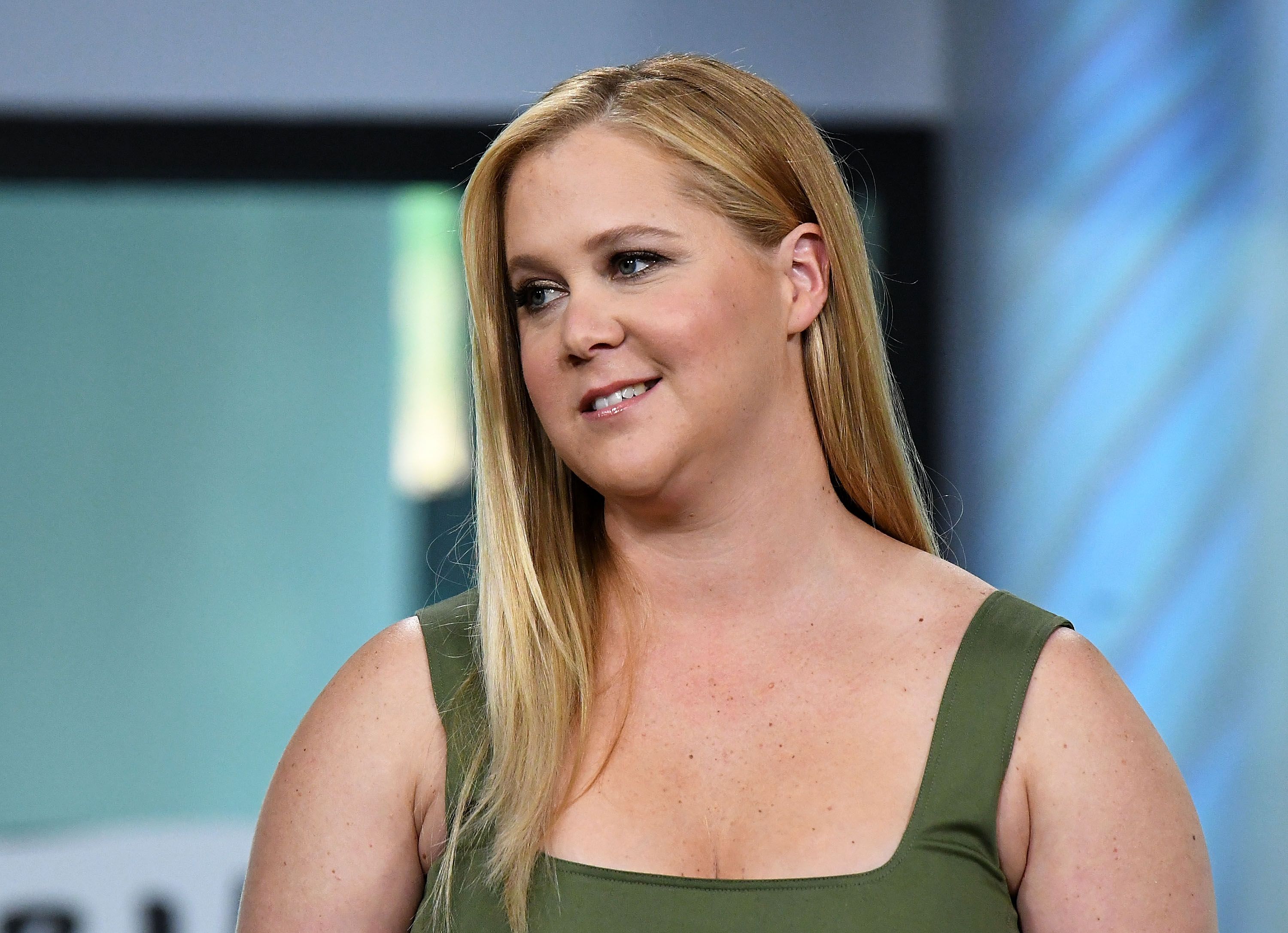 Amy Schumer appears on "Build Series" while promoting her film "Snatched." She wears a sleeveless green dress with her hair styled long and straight.