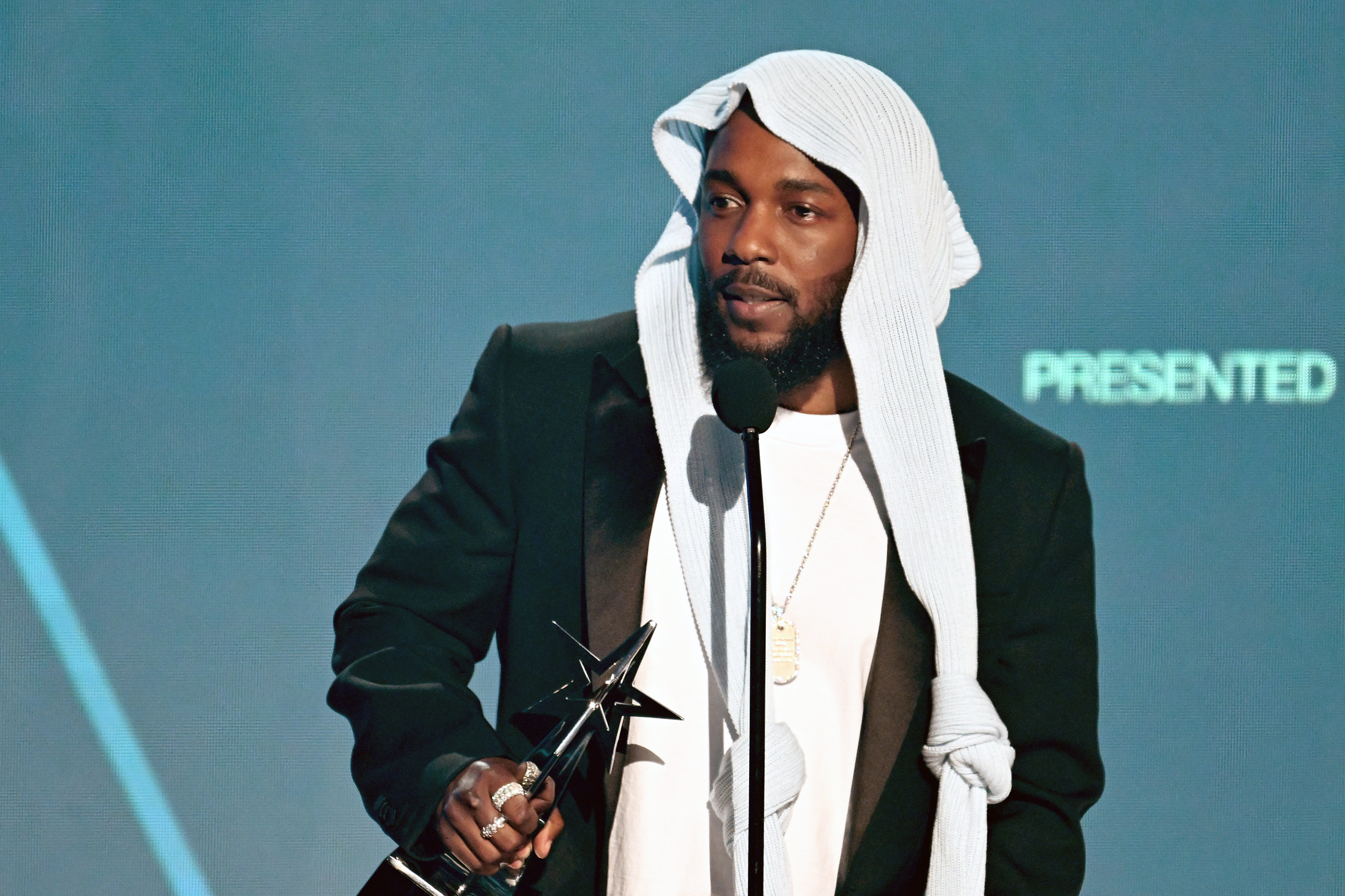 Speaking to the crowd, Kendrick Lamar delivers a heartfelt message while accepting an award at the 2025 BET Awards, held at the Peacock Theater. His unconventional head covering continued to draw attention during his time at the mic.