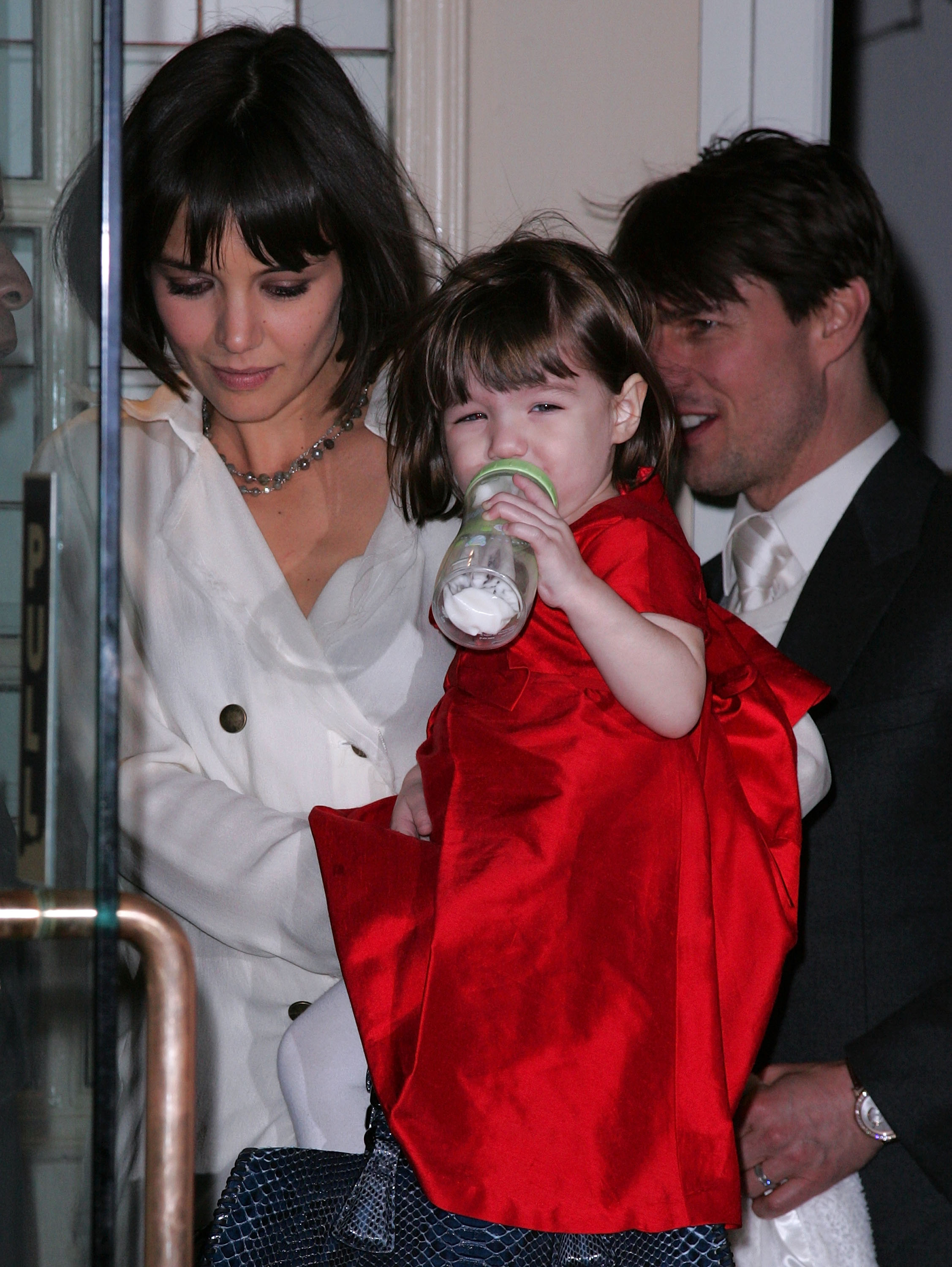 Katie Holmes carried Suri Noelle while Tom Cruise walked beside them during an outing in New York on January 14, 2008. Wearing a bright red dress and holding a bottle, the toddler was photographed during her early years in the public eye, when the family was still frequently seen together before Tom and Katie's 2012 divorce.