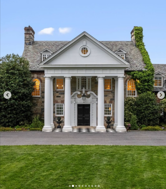 Longmeadow's stately entrance sets the tone with four white columns, a black front door, stonework, and ivy climbing the facade. The manicured lawn reinforces the formal character of the 1929 Georgian-style estate. | Source: Instagram/rogerperrygroup