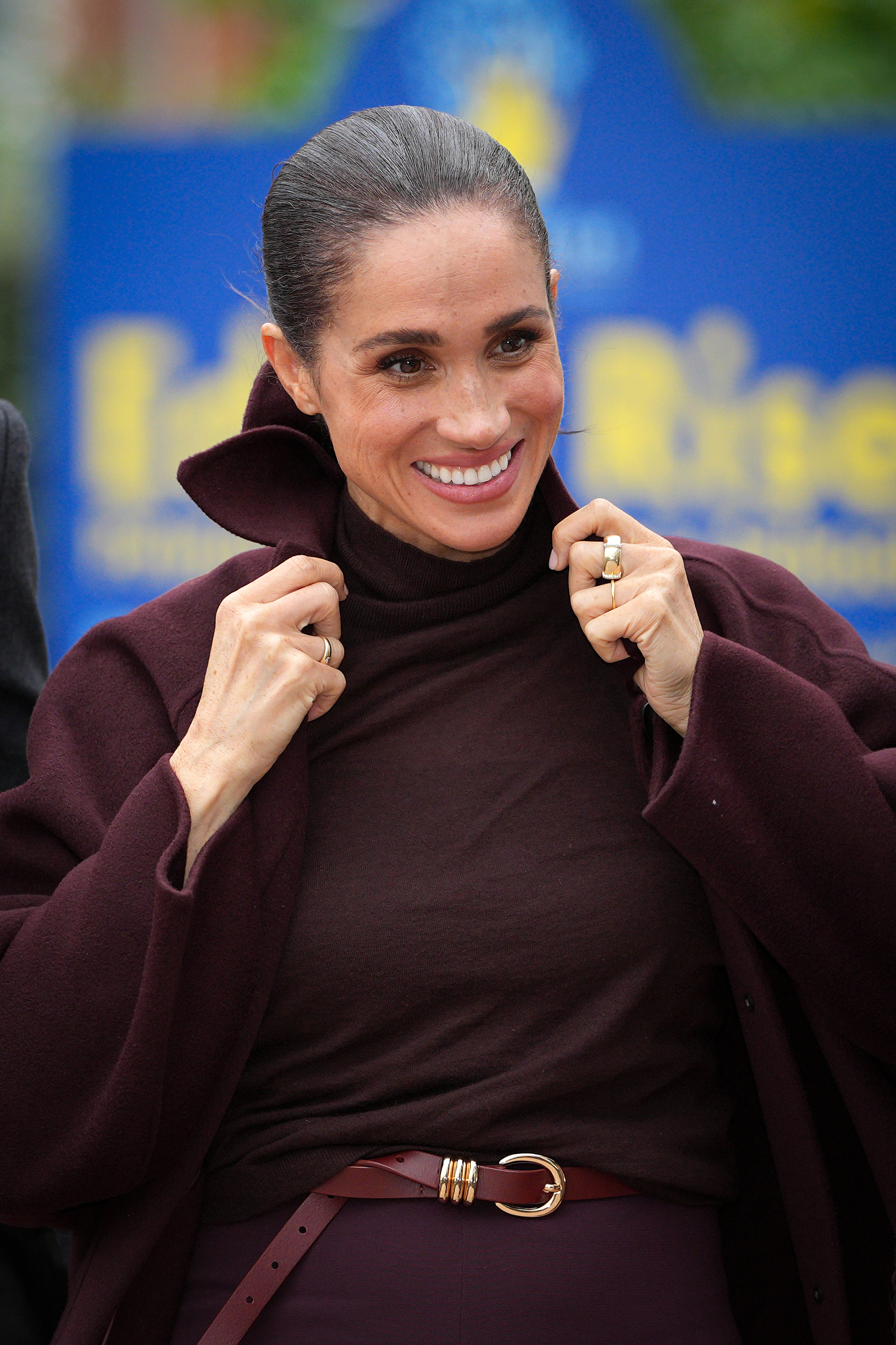 Meghan, Duchess of Sussex, adjusts the upturned collar of her tailored burgundy coat as she arrives at Epic Partners in Nottingham, England, on October 15, 2026, styling the rich monochromatic look with a matching turtleneck sweater and a belted waistband. | Source: Getty Images