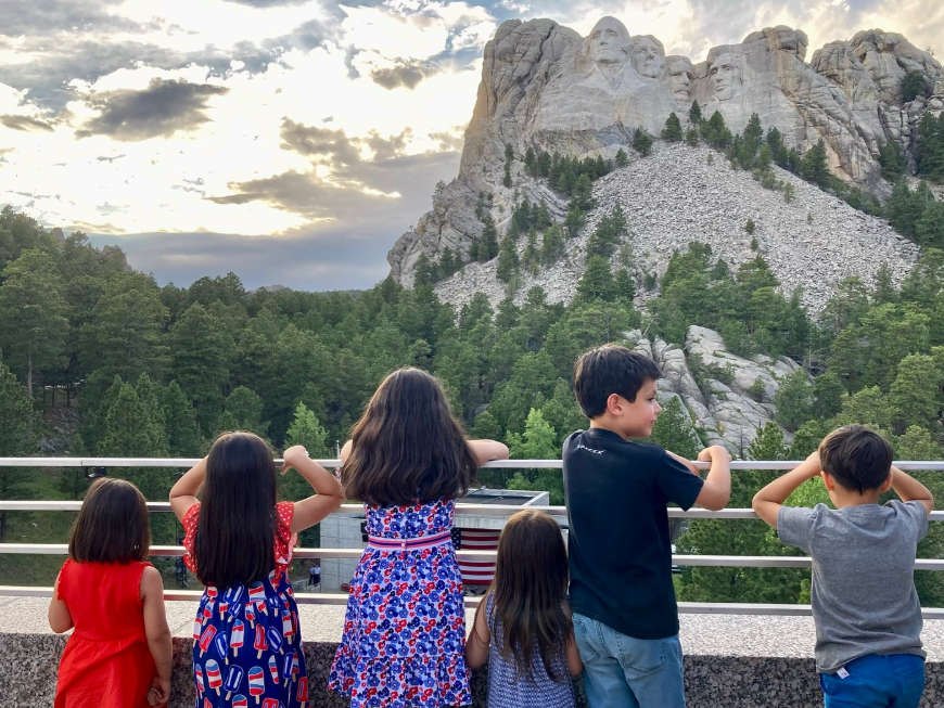 Ewan, Vivek, and Mirabel Vance along with other young children stand with their backs to the camera, leaning against a railing as they look out toward Mount Rushmore in the distance. | Source: Instagram/vp