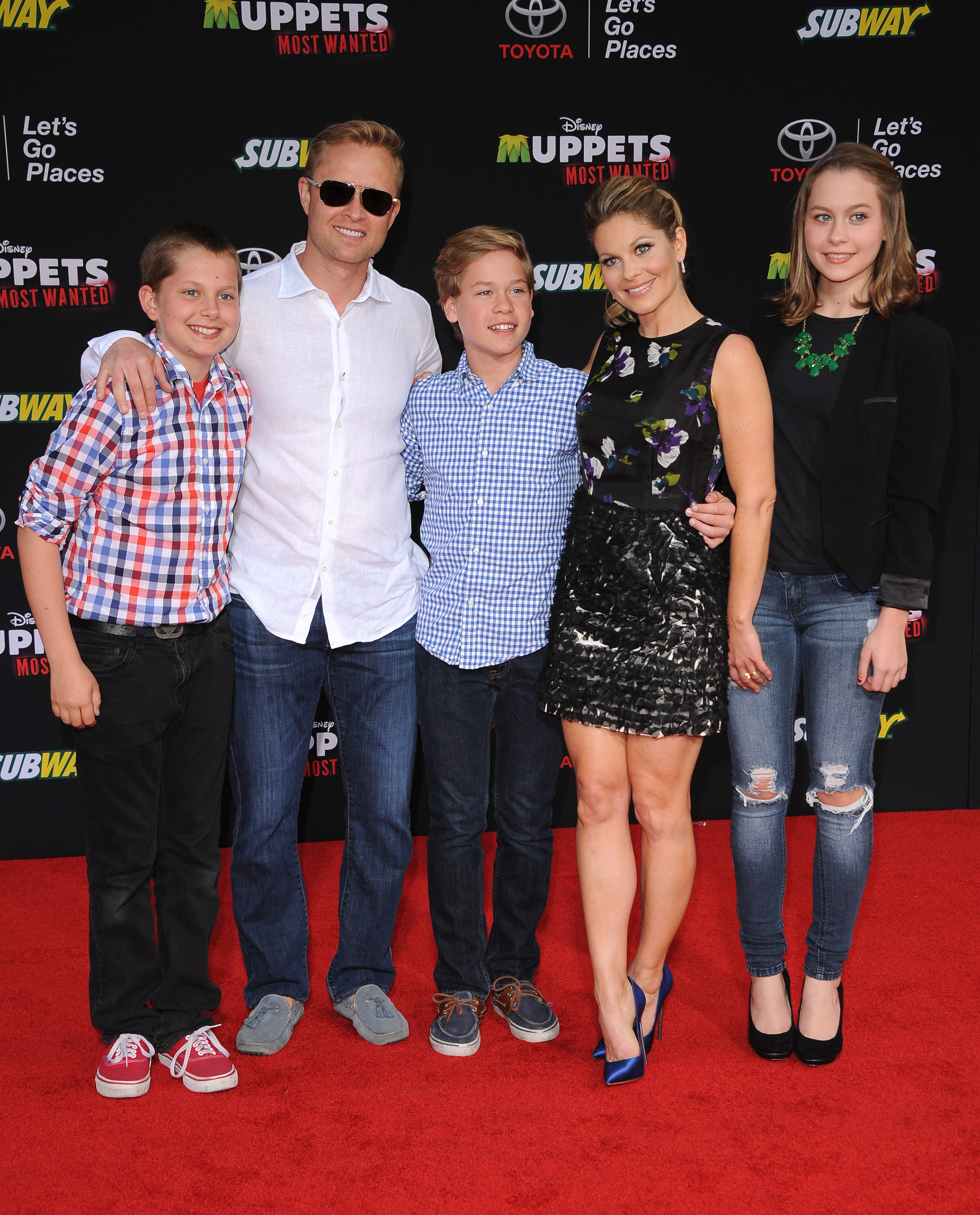 Candace Cameron Bure steps out with husband Valeri Bure and their children—Lev, Maksim, and Natasha—at the Los Angeles premiere of "Muppets Most Wanted" at the El Capitan Theatre on March 11, 2014, in Hollywood, California. The actress stuns in a patterned sleeveless mini dress and bright blue satin pumps, flanked by daughter Natasha in distressed denim and a black blazer, while youngest son Maksim beams in the center wearing a blue gingham button-down shirt and dark jeans. | Source: Getty Images