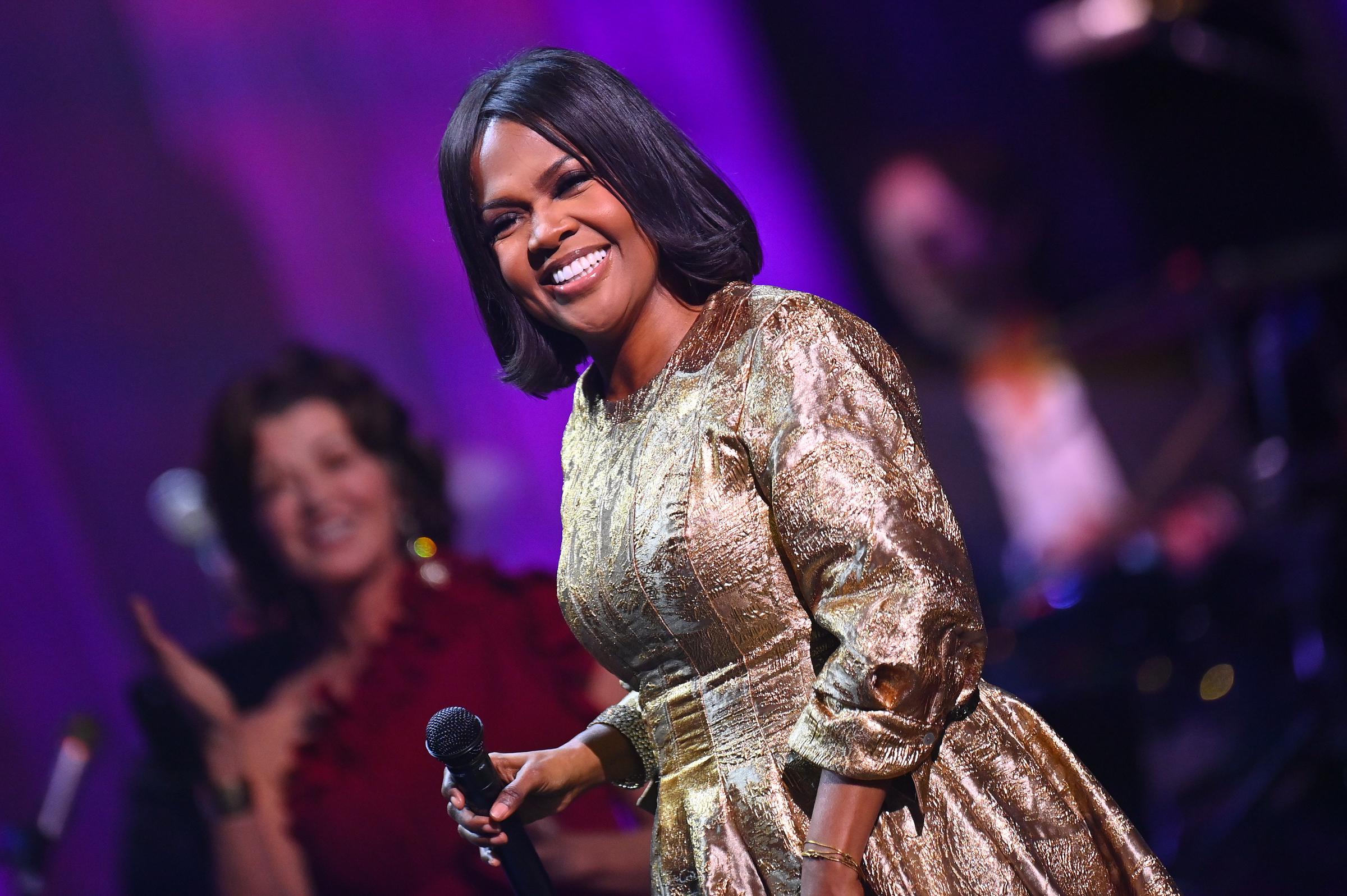CeCe Winans smiles while holding a microphone during the "Christmas Together" tour at The Fox Theatre in Atlanta, Georgia, on December 6, 2025, wearing a gold stage outfit.