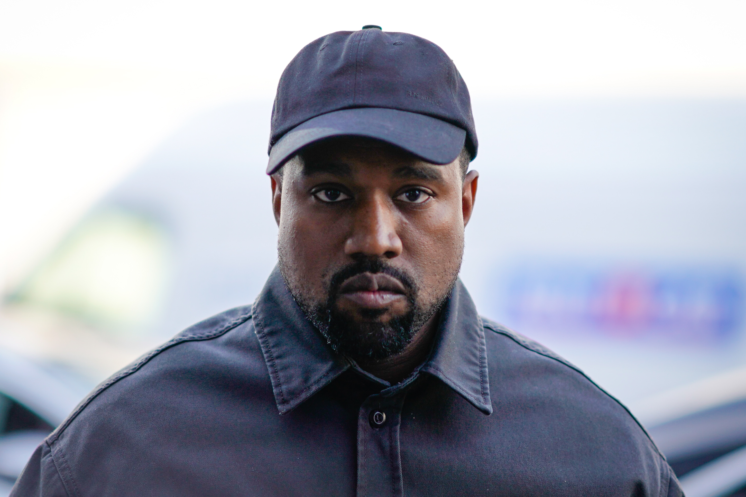 Kanye West fixed an intense, direct gaze toward the camera outside the 1017 ALYX 9SM Menswear Spring/Summer 2019 presentation during Paris Fashion Week on June 24, 2018, in Paris, France. Sporting a trimmed beard and a subdued, utilitarian aesthetic, the music and design icon paired a washed charcoal collared jacket with a matching curved-brim baseball cap pulled low over his forehead. | Source: Getty Images