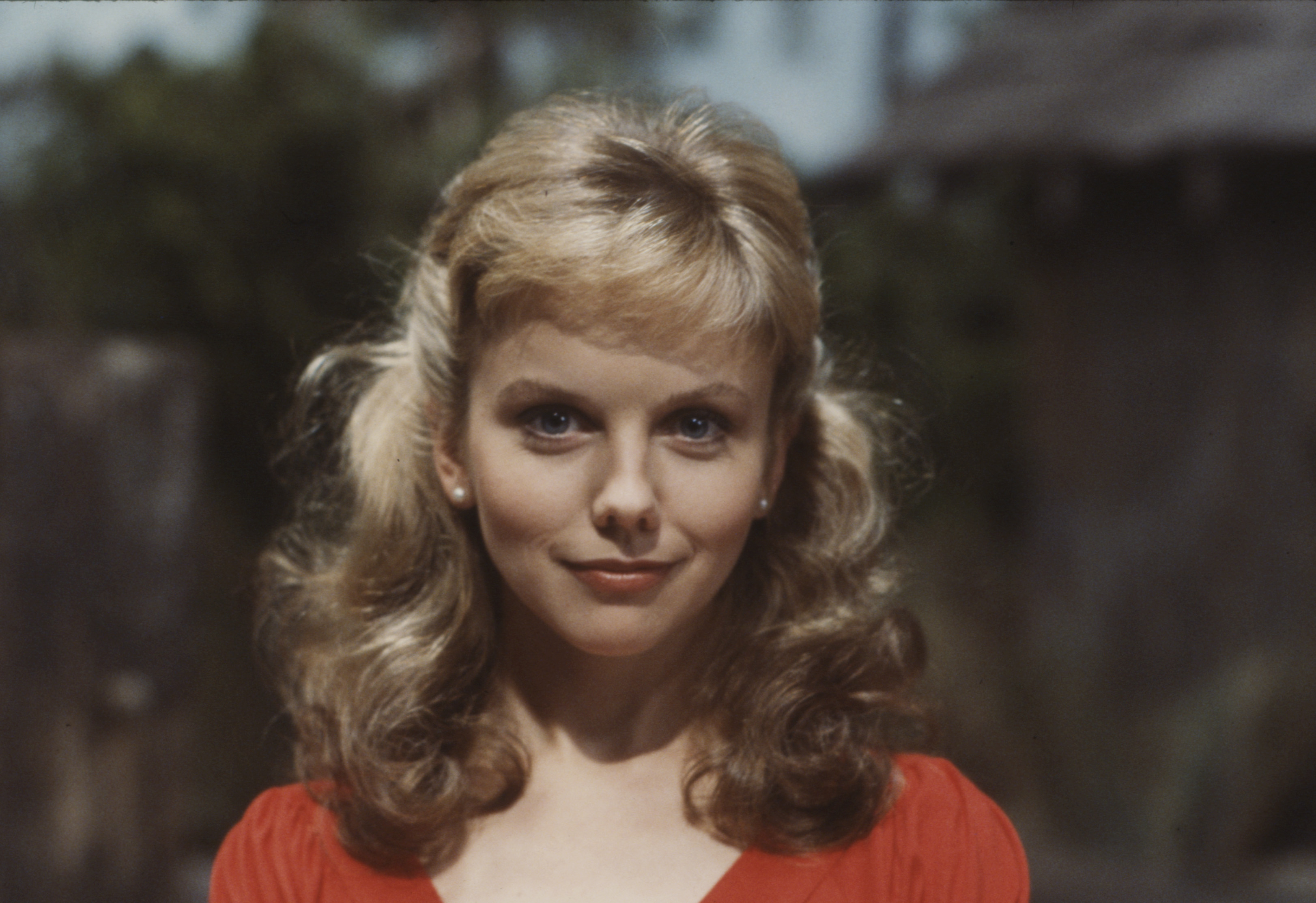 A vibrant cherry-red dress with puffed shoulders gave 27-year-old Linda Purl an unmistakable girl-next-door innocence during this 1983 promotional shoot for the unaired pilot "Weekend". With her golden-blonde locks swept into a half-updo of bouncy ringlets, delicate pearl earrings set off her bright blue eyes and subtle, youthful smirk.