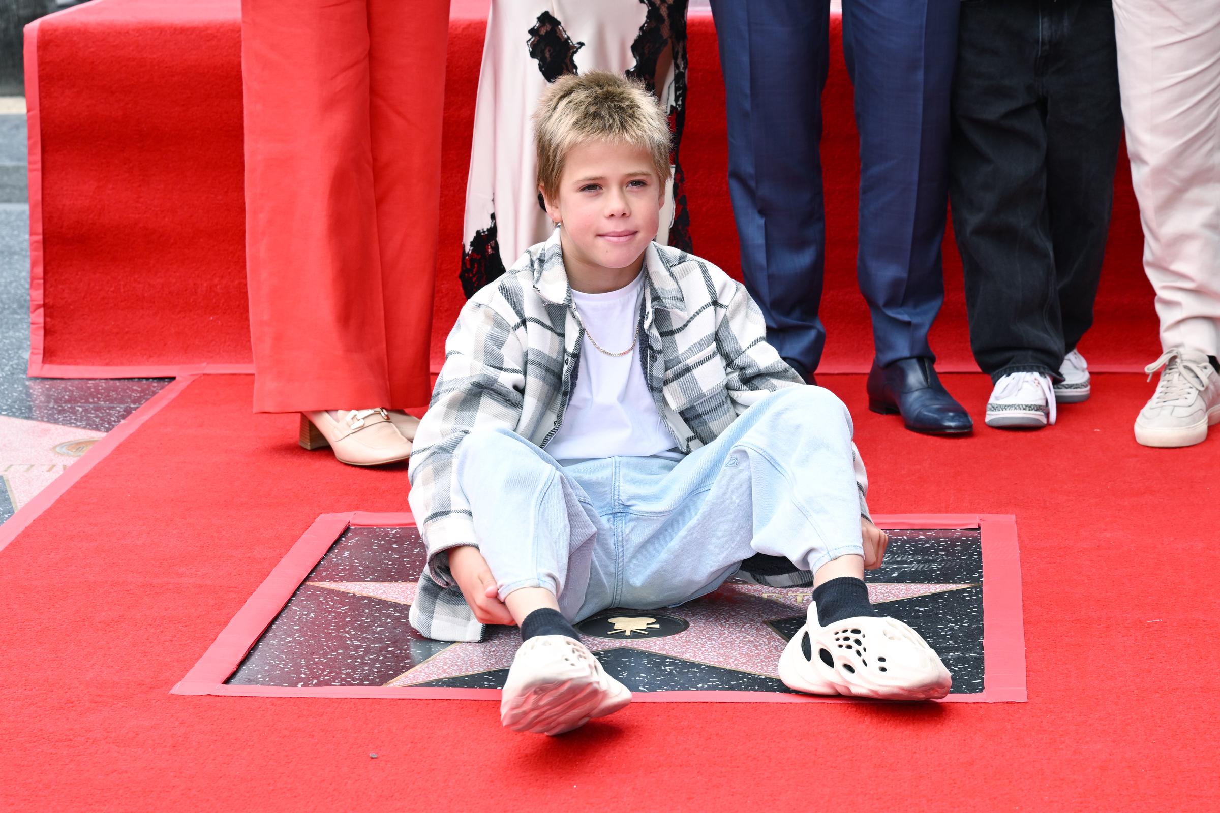 Sasha Hemsworth sits on the red carpet, directly above Chris Hemsworth's newly unveiled Hollywood star. Wearing a plaid shirt, white tee, and light-wash jeans, the young boy smiled calmly for cameras during the family celebration.