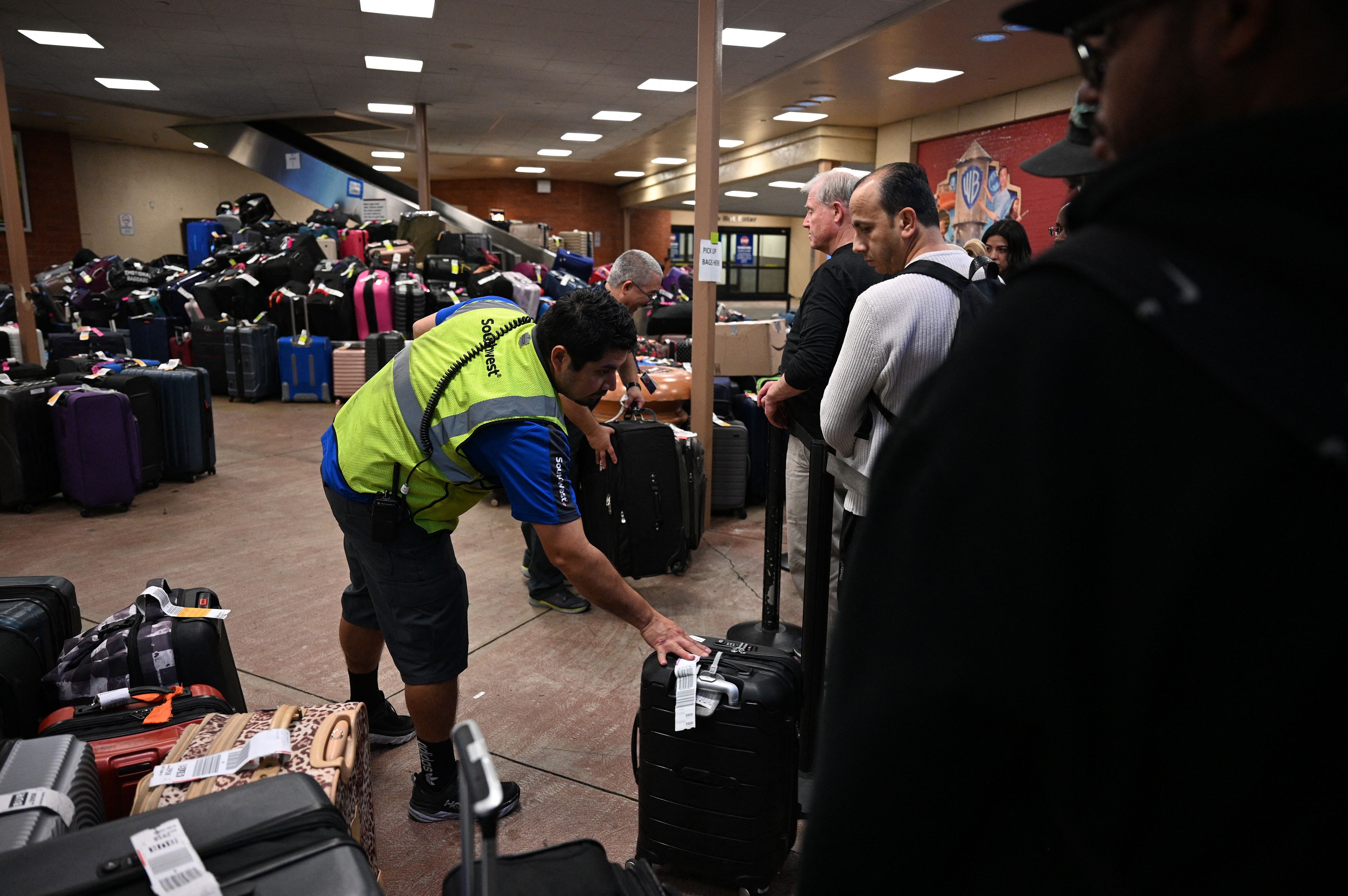 An airline employee pass luggage to passengers at a baggage carousel at Hollywood Burbank Airport on December 27, 2022 | Source: Getty Images