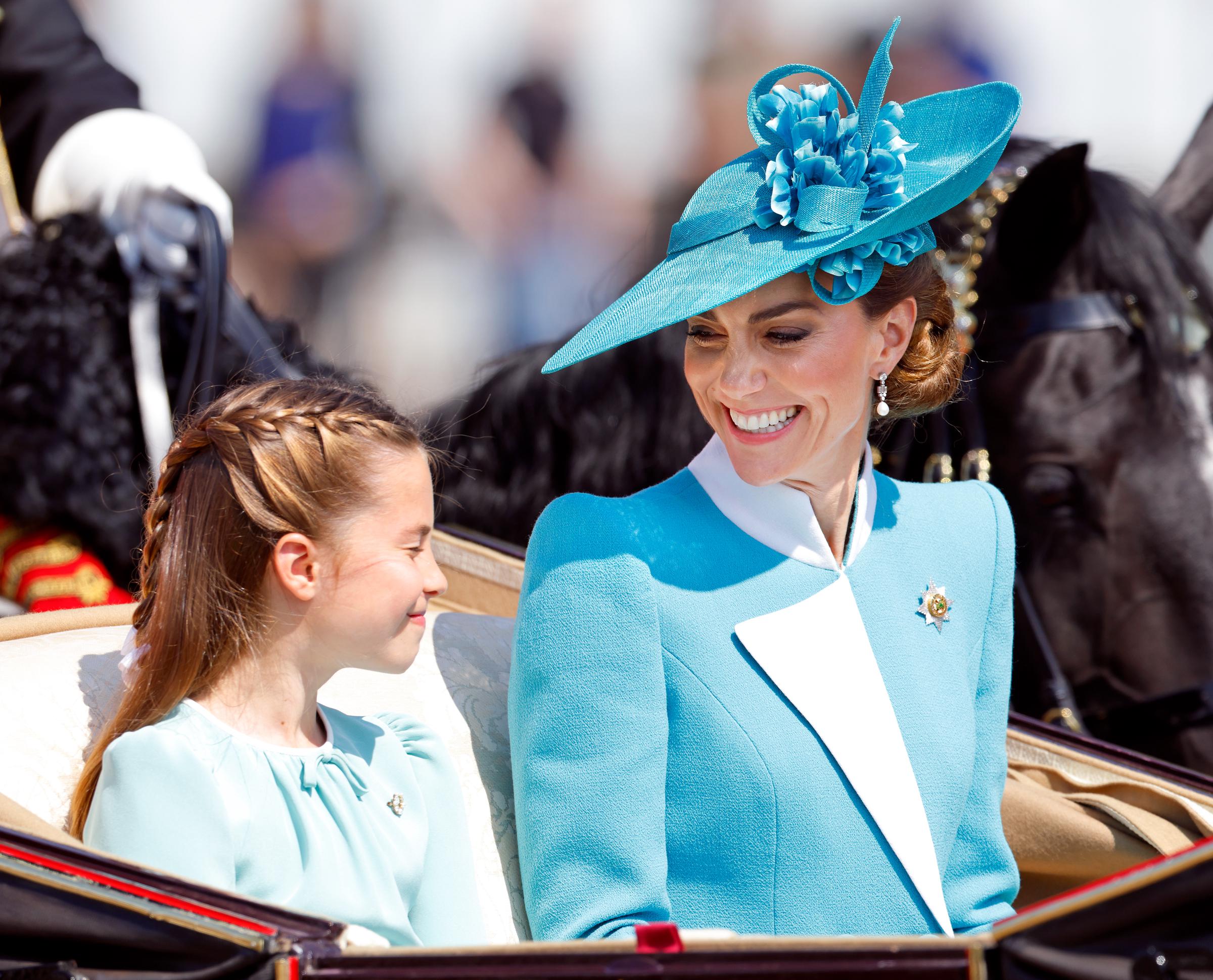 Princess Charlotte of Wales and Catherine, Princess of Wales smile at each other as they depart Buckingham Palace in a horse-drawn carriage during the 2025 Trooping The Colour parade.