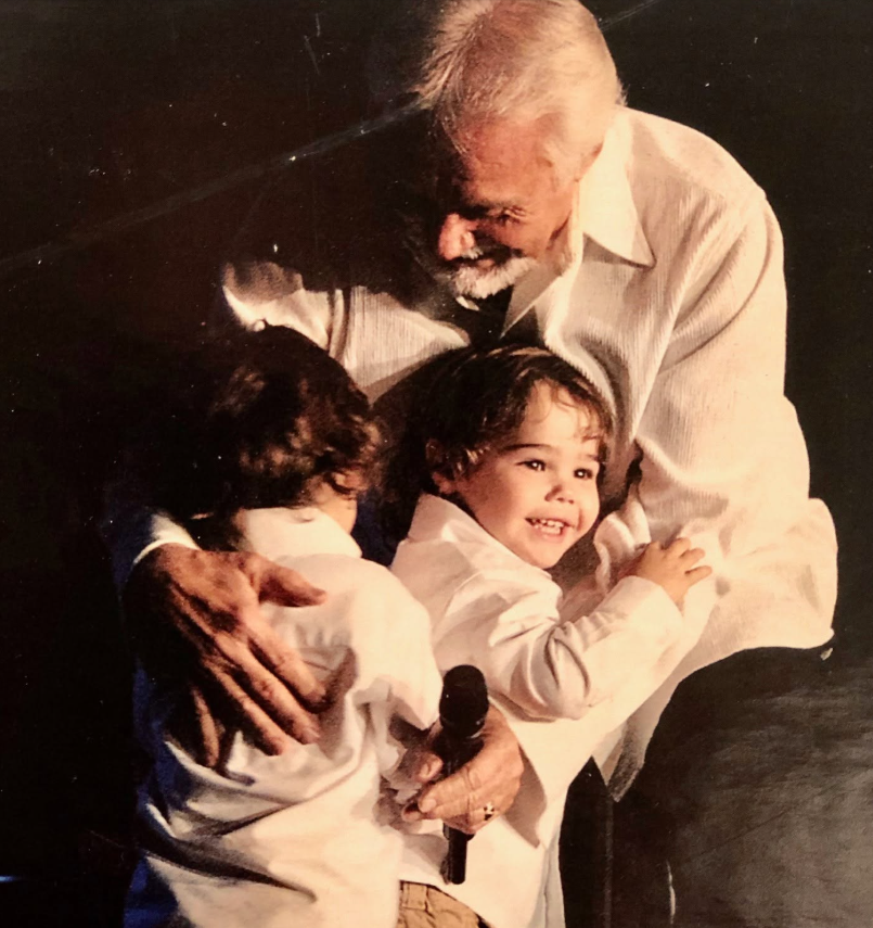 This tender throwback photo captures Kenny Rogers embracing his twin sons onstage, offering an early glimpse of the father-son bond behind the family resemblance debate that would follow the boys into adulthood. | Source: Facebook/Kenny Rogers