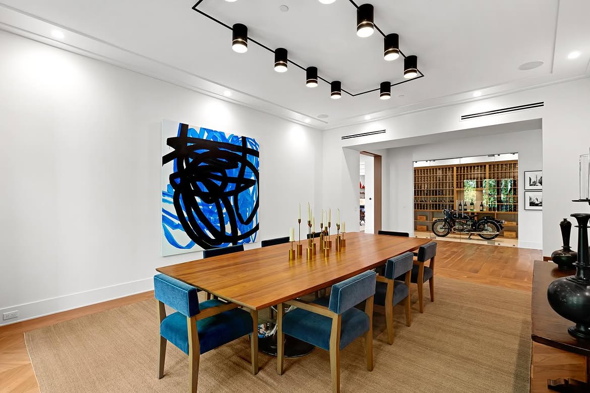The dining room's blue seating and large abstract artwork introduce bolder color than most of the surrounding spaces. Beyond the table, an open doorway offers a first glimpse of one of the home's most unusual displays. | Source: Instagram/theshevins